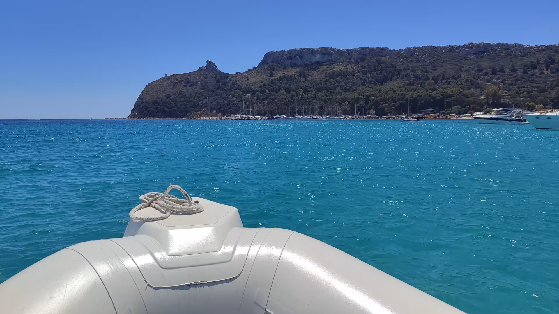 Explore Cagliari's stunning coastline on a dinghy tour with views of crystal-clear blue waters and rugged hills.
