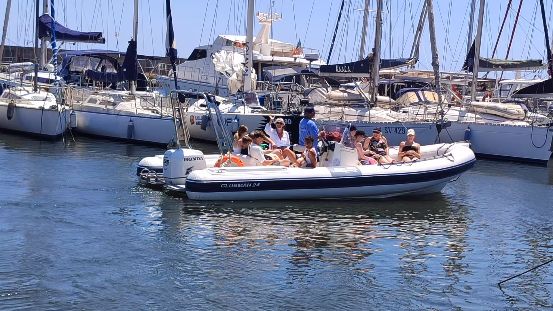 Experience vibrant Cagliari harbor life with a group on a dinghy tour, surrounded by sailboats and sunny weather.