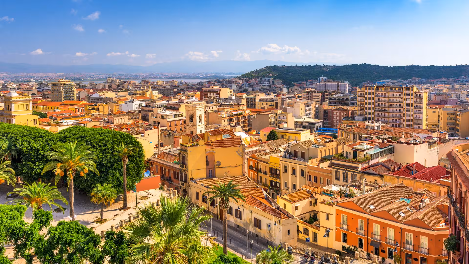 Panoramic view of Cagliari's historic center with colorful architecture and lush greenery under a clear blue sky.