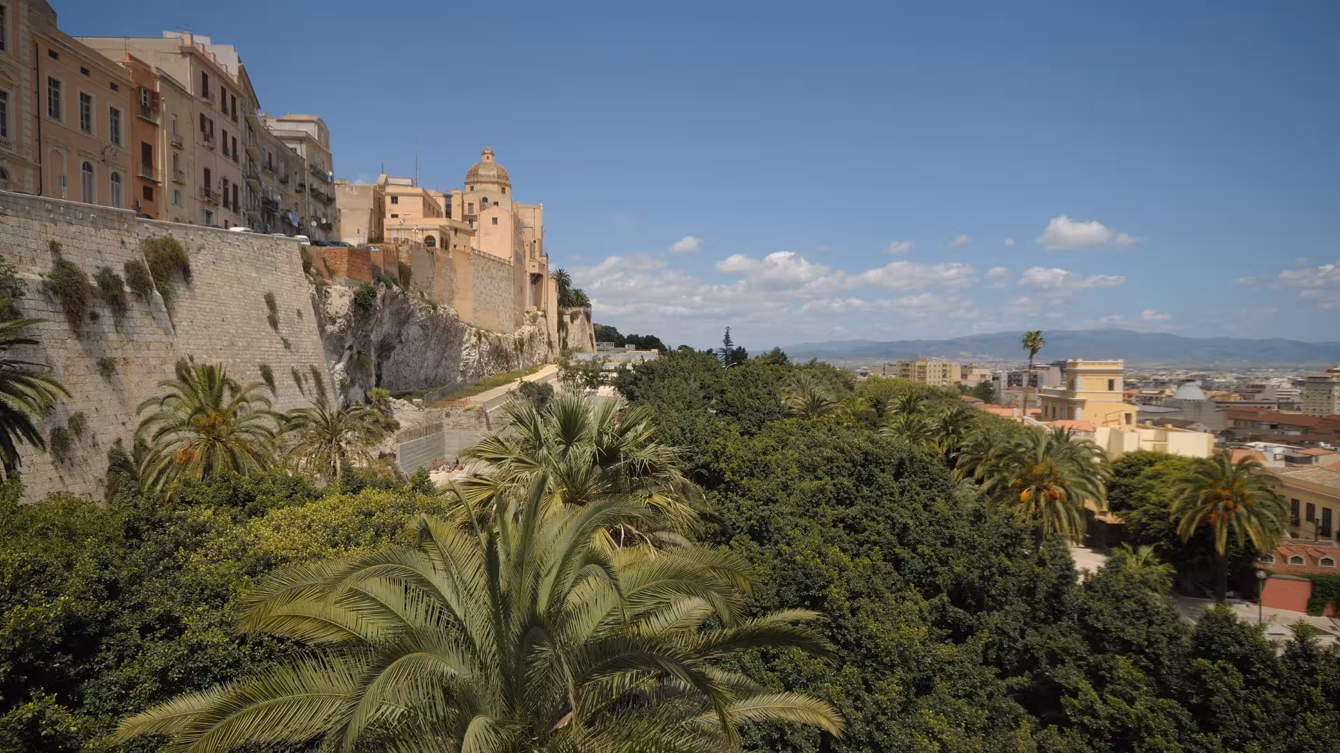 Panoramic view of Cagliari's historic district with lush greenery and ancient architecture under a bright blue sky.