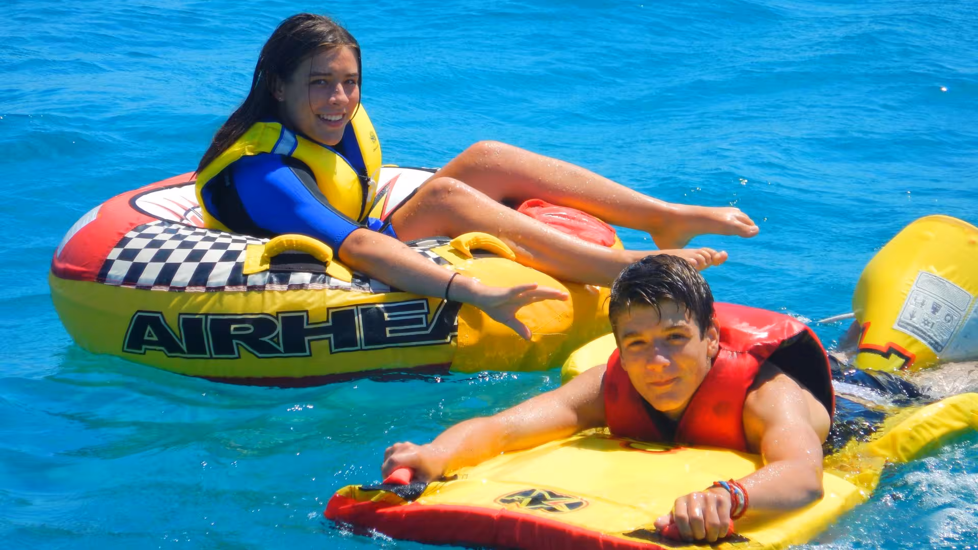 Excited duo riding inflatable tubes on the crystal-clear waters of Golfo degli Angeli, Cagliari.