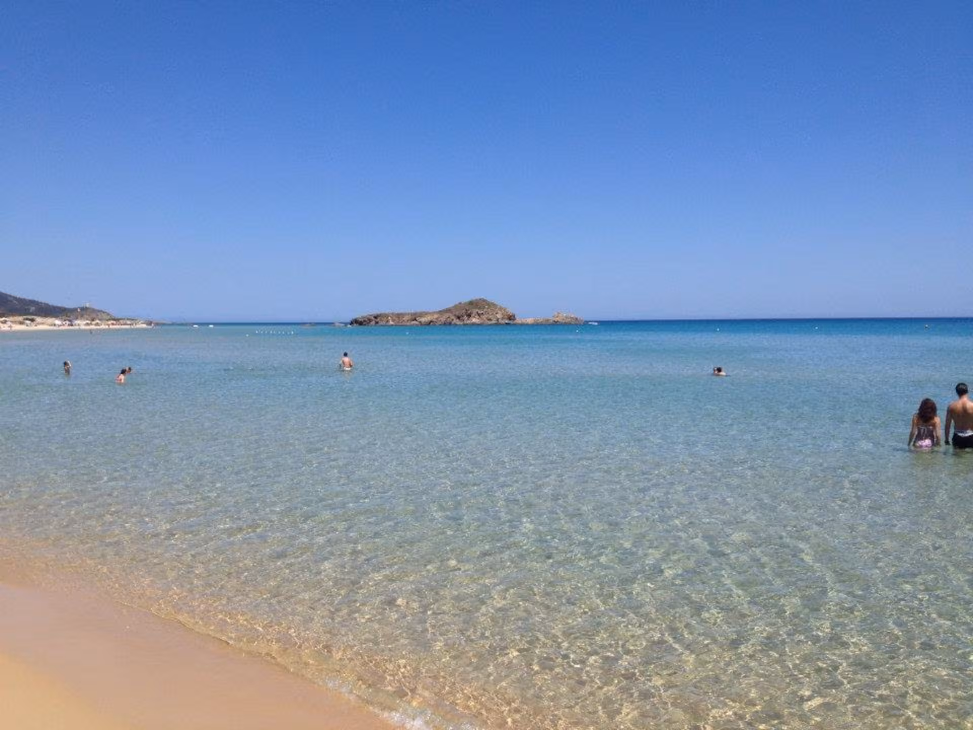 People enjoying the clear, turquoise waters at Chia Beach, perfect for swimming on the Cagliari jeep tour.