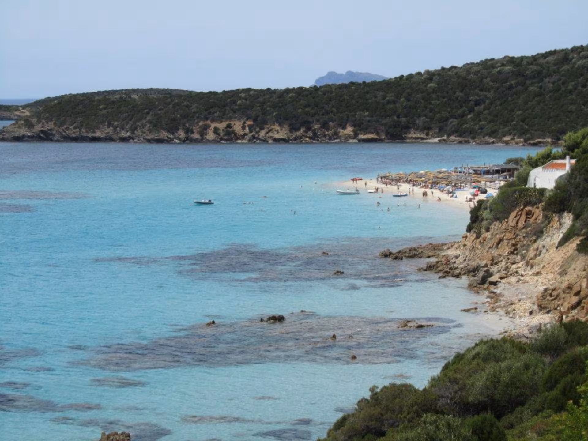 Chia beach scene with sunbathers and crystal-clear waters, highlighting a must-visit spot on a Cagliari jeep tour.