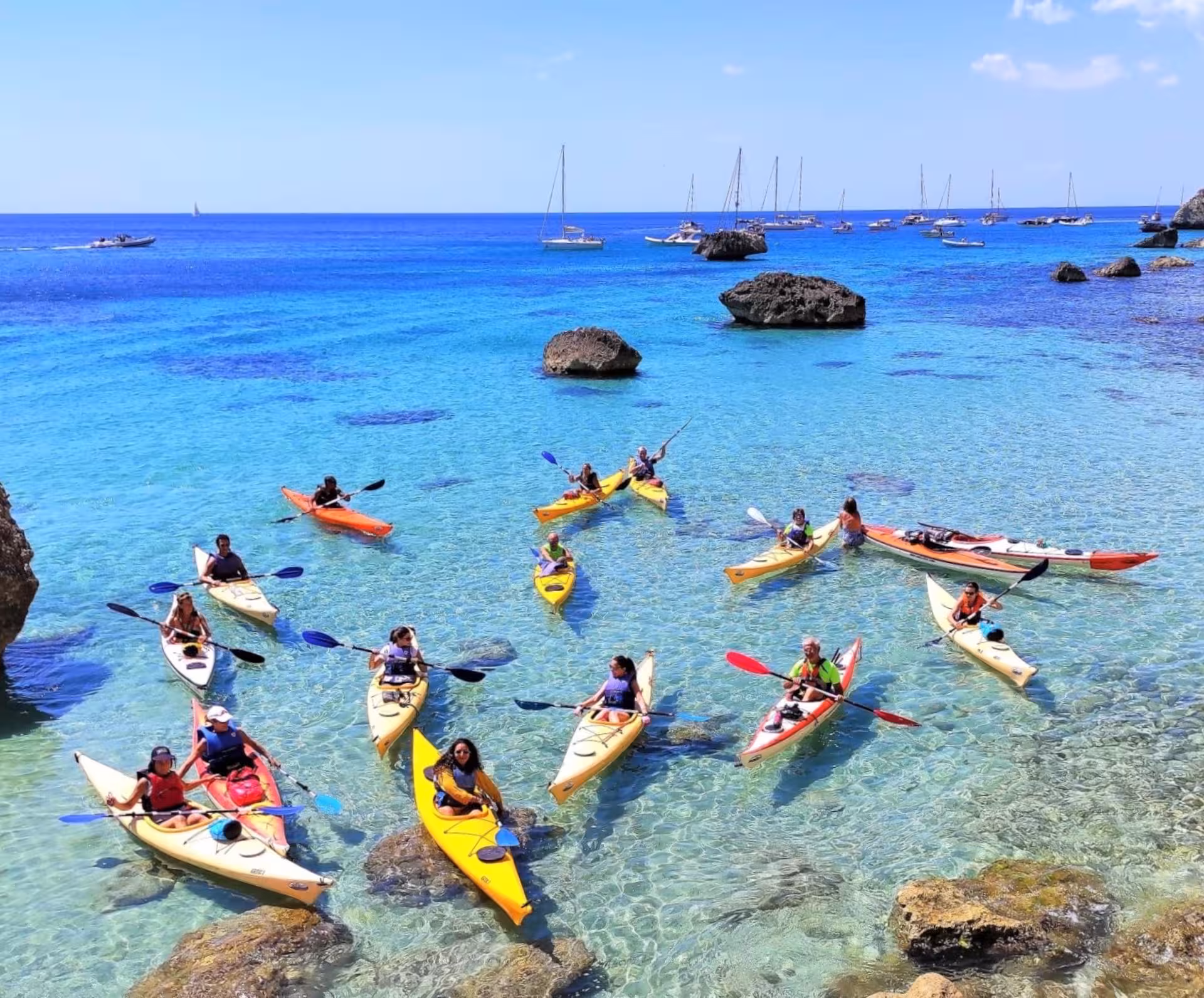 Aerial view of kayakers exploring the vibrant blue waters of Cagliari with sailboats in the background.