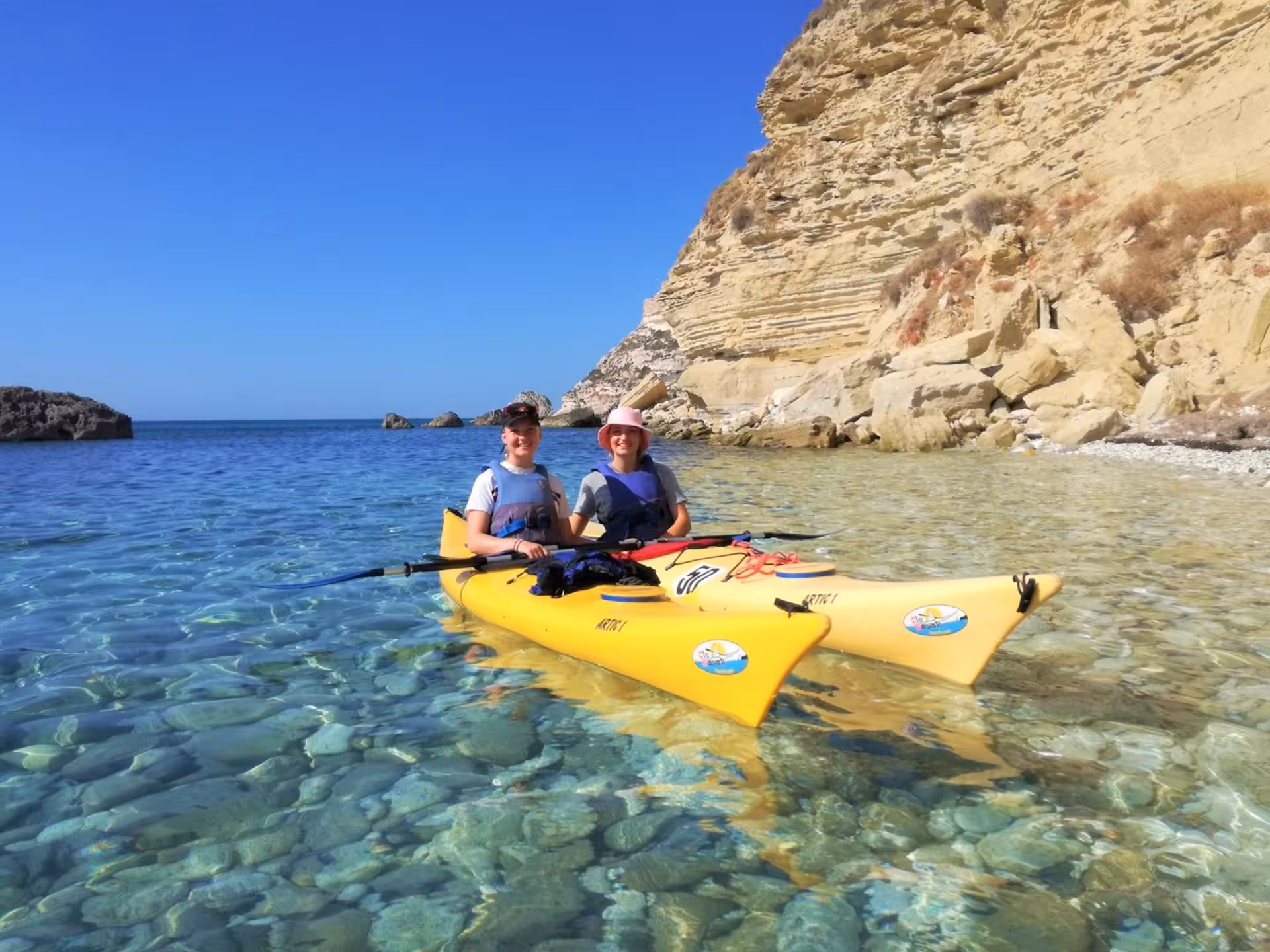 Two kayakers in yellow kayaks enjoying the serene, clear waters and rocky coastline of Cagliari.