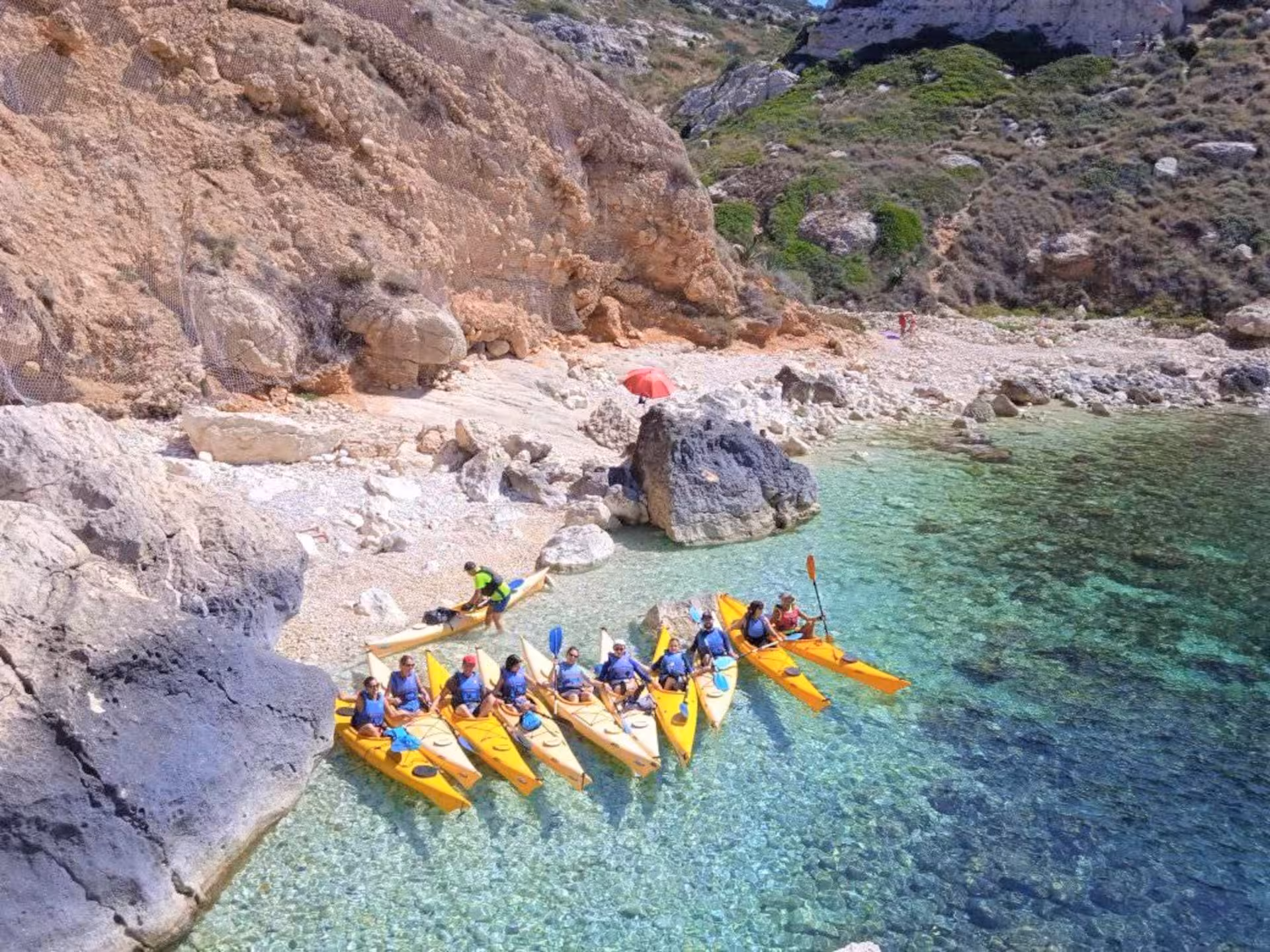 Group of kayakers relax on a secluded beach with crystal-clear waters during a Cagliari kayak tour.