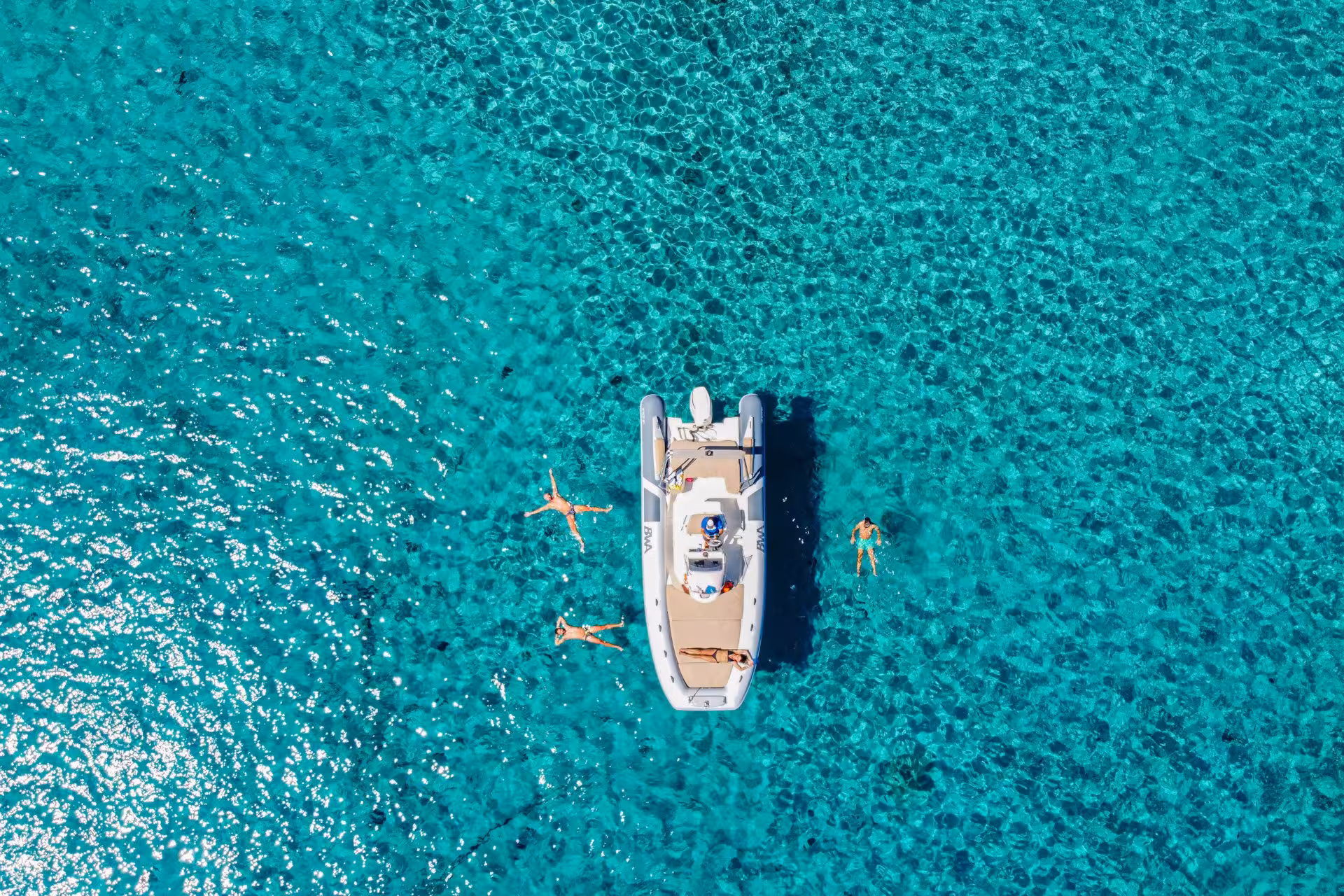 Top view of a RIB boat with people swimming in the vibrant blue sea of Cagliari, highlighting the beauty of a coastal tour.