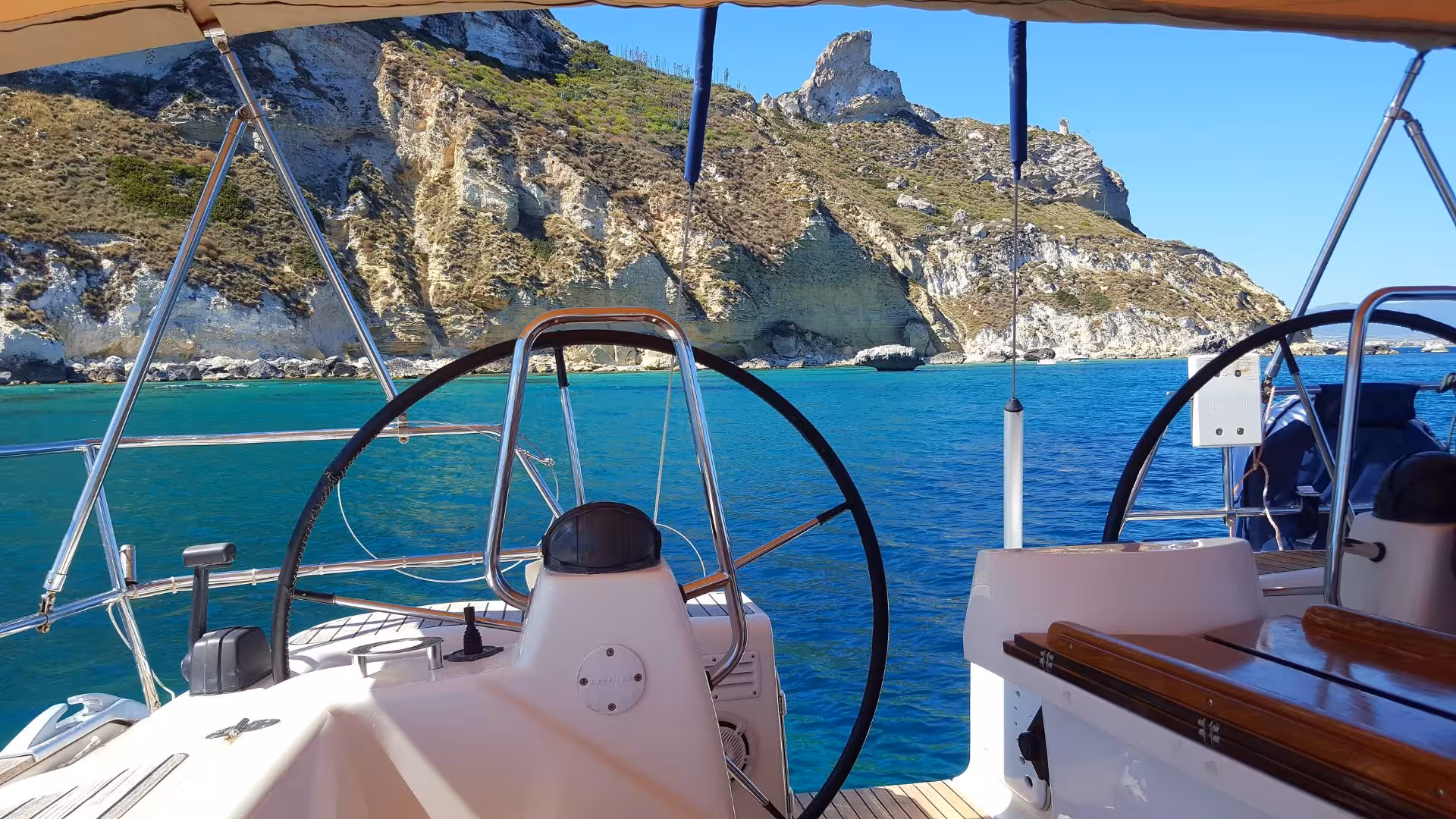 View from the helm of a sailing boat on a crystal-clear tour in Cagliari, showcasing stunning coastal cliffs.
