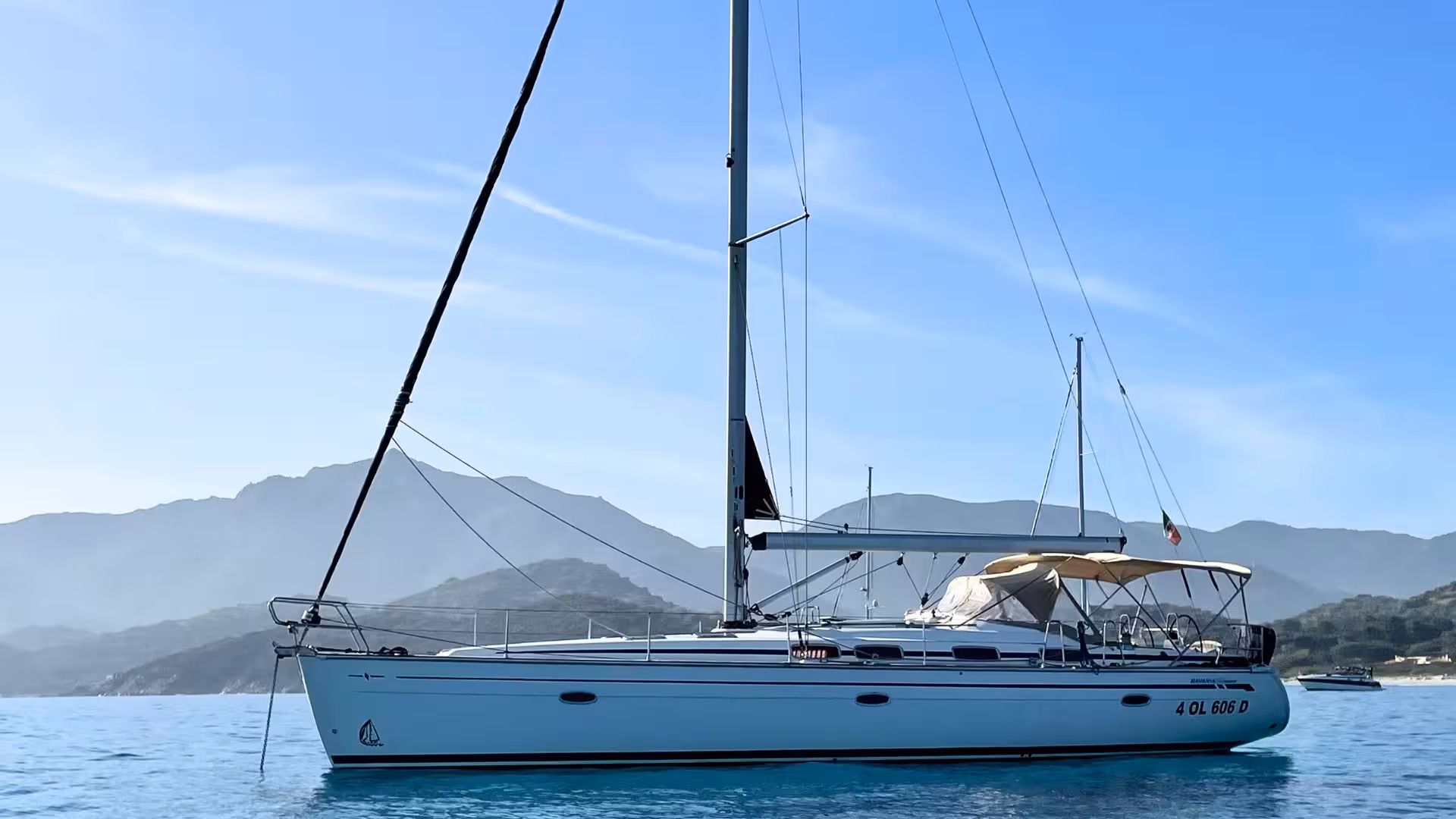 Elegant sailing boat on the tranquil blue waters of Cagliari with mountainous backdrop, perfect for a Mari Pintau tour.