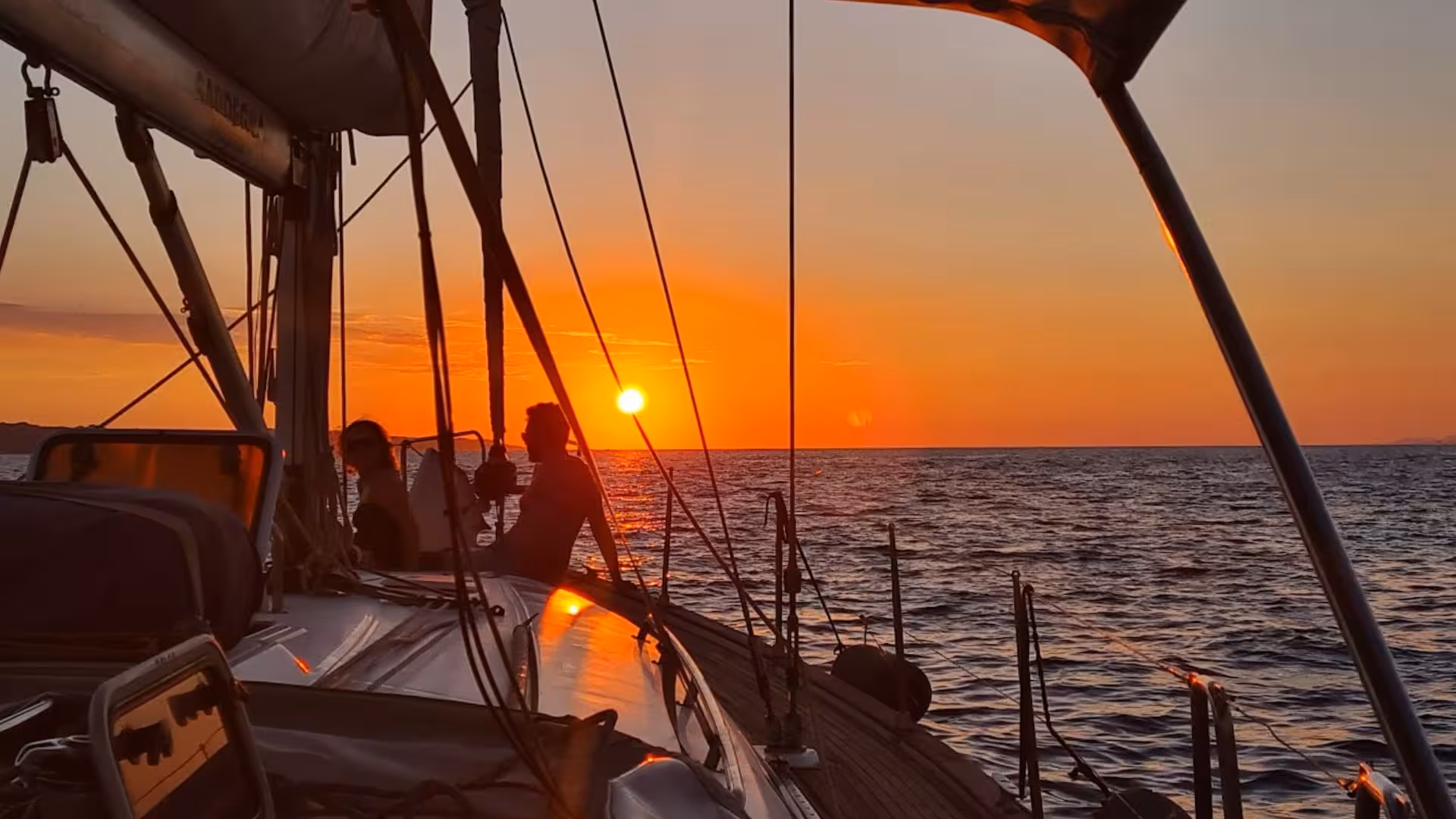 Silhouette of people on a sailing boat during a vibrant sunset on a Cagliari 5-hour sailing tour.