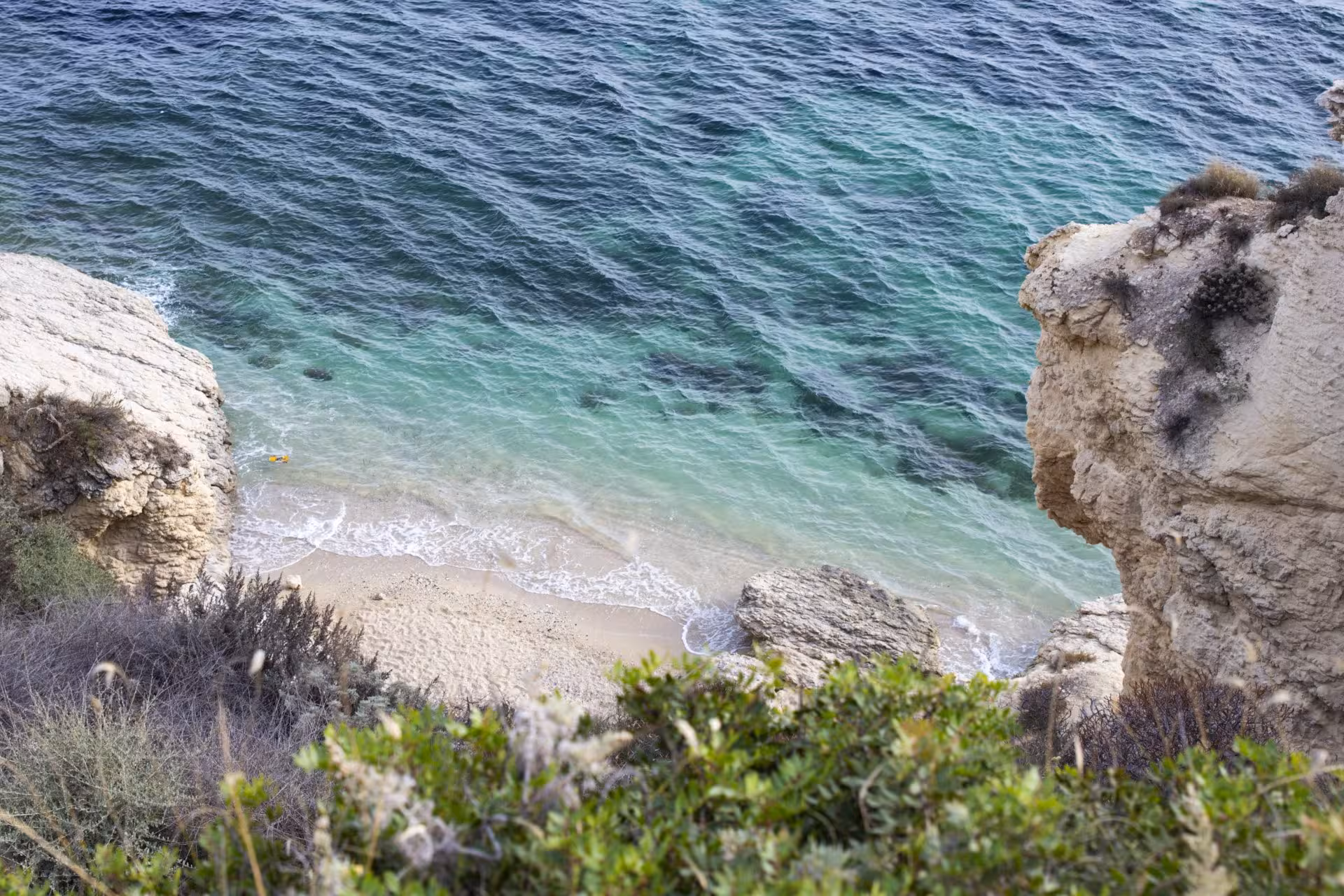 Aerial view of Sant'Elia hill's rocky coastline with turquoise waters and sandy beach in Cagliari at sunset.