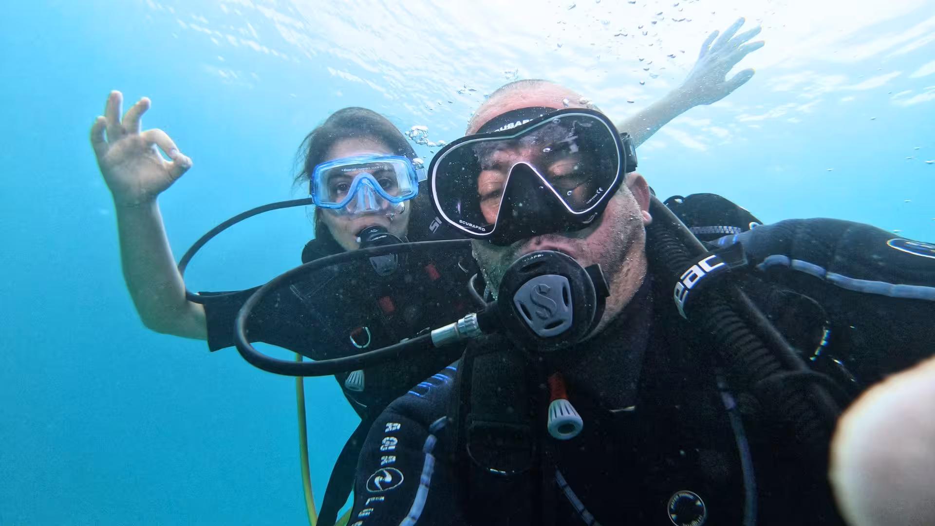 Two scuba divers explore underwater in Cagliari, signaling OK for a beginner-friendly diving experience.