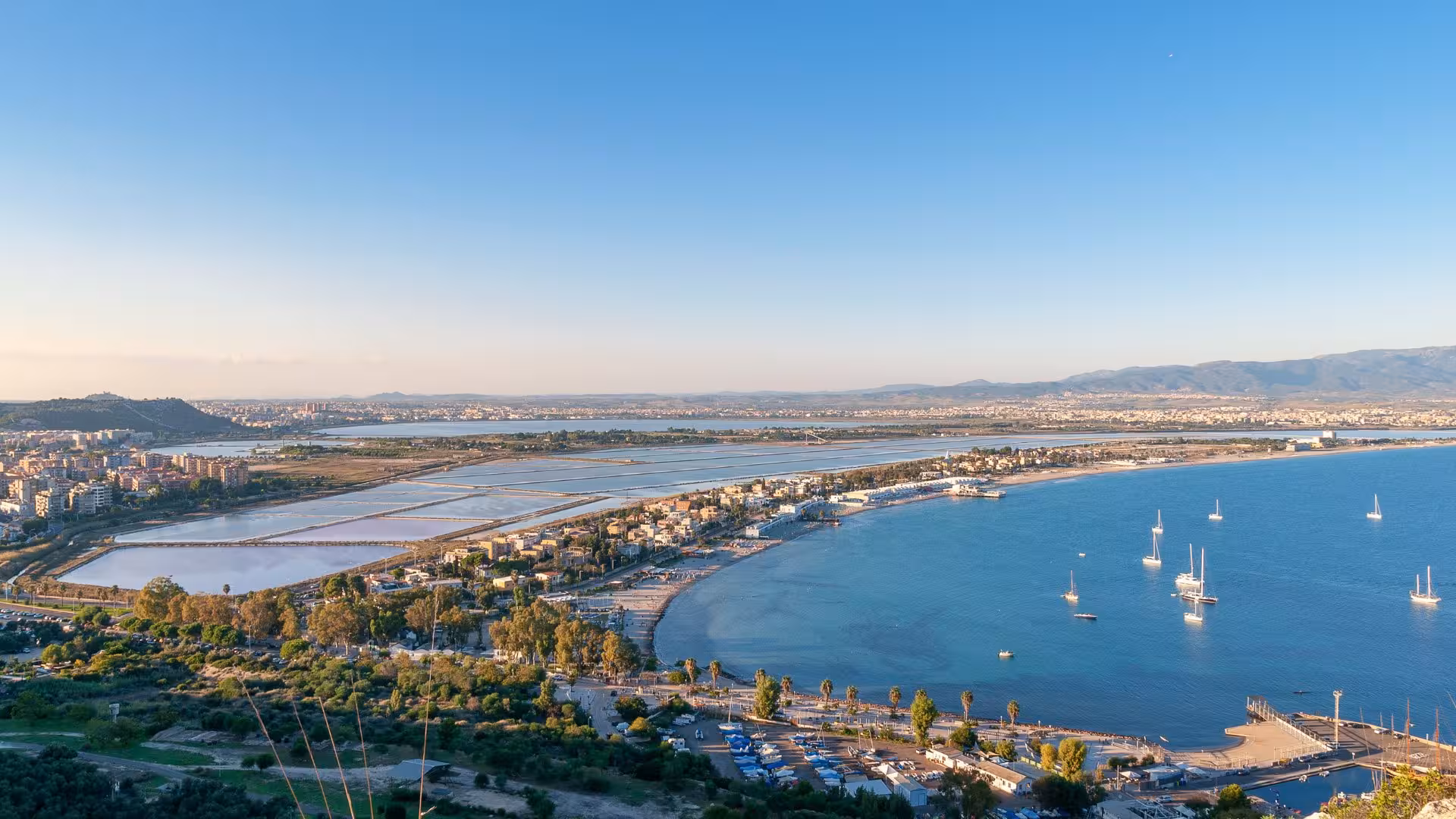Aerial view of Cagliari's coastline and marina, showcasing vibrant cityscape and tranquil blue sea perfect for trekking tours.