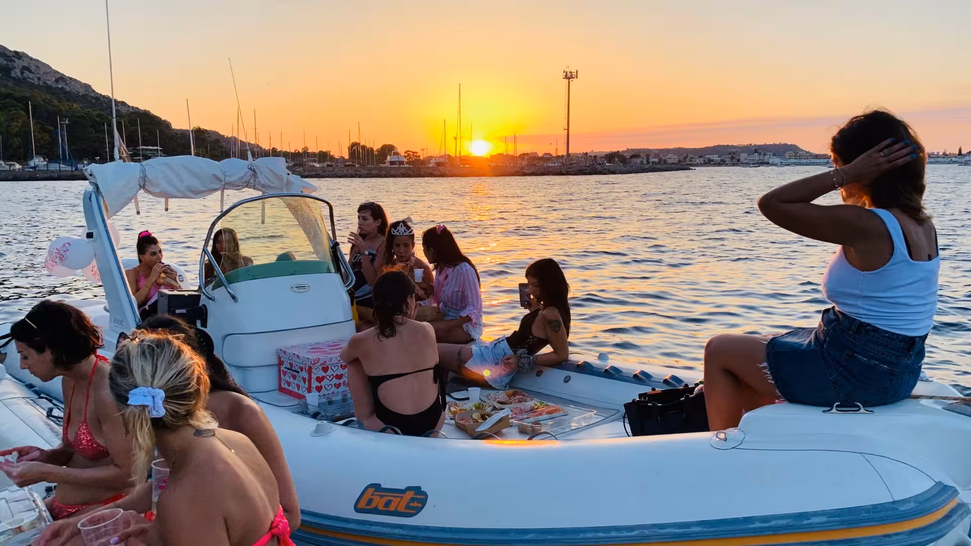 Group enjoying a sunset aperitif on a dinghy near Cagliari, with vibrant skies and picturesque sea views.