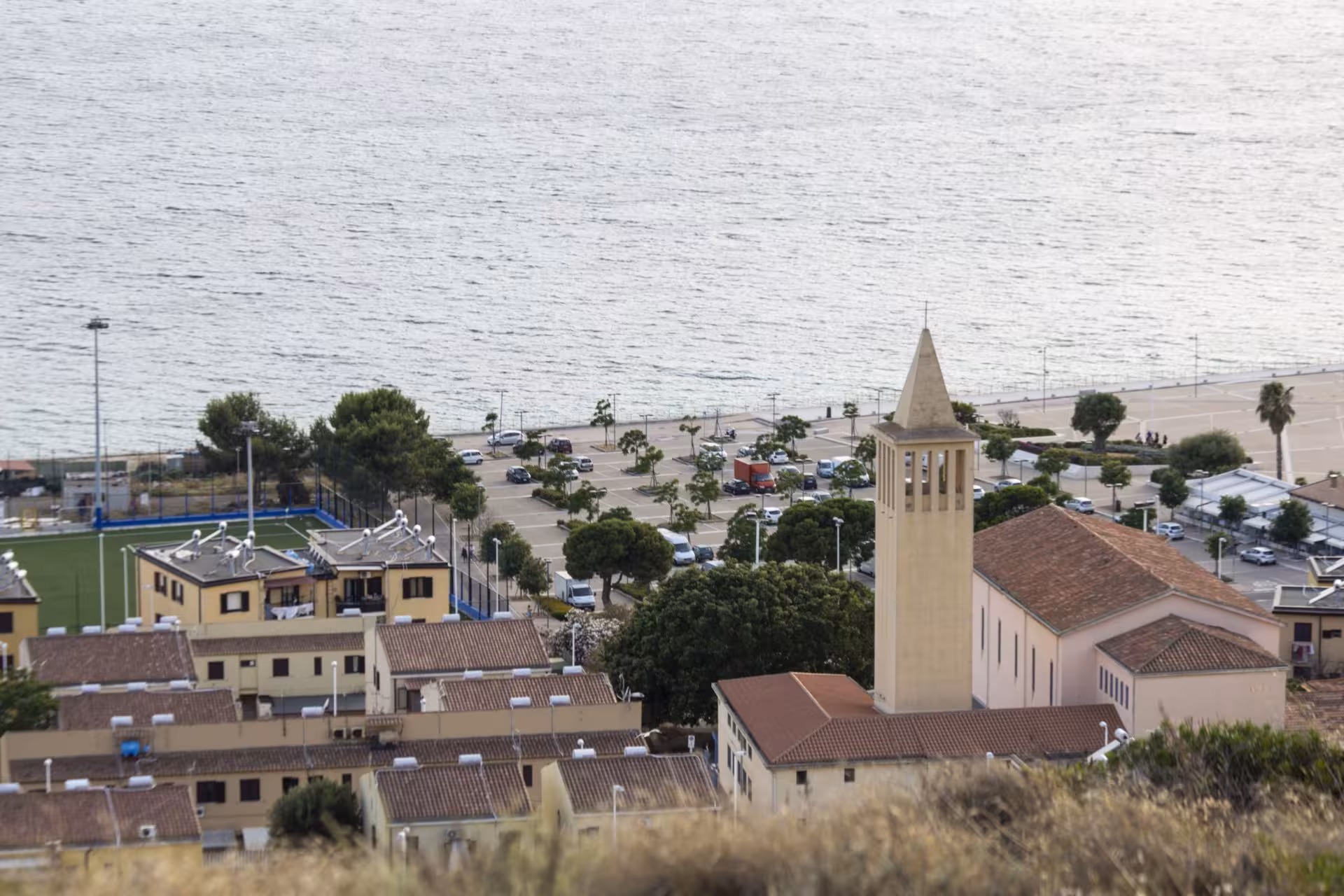 Scenic view of Cagliari's waterfront from Sant'Elia hill, featuring a church tower and coastal landscape.
