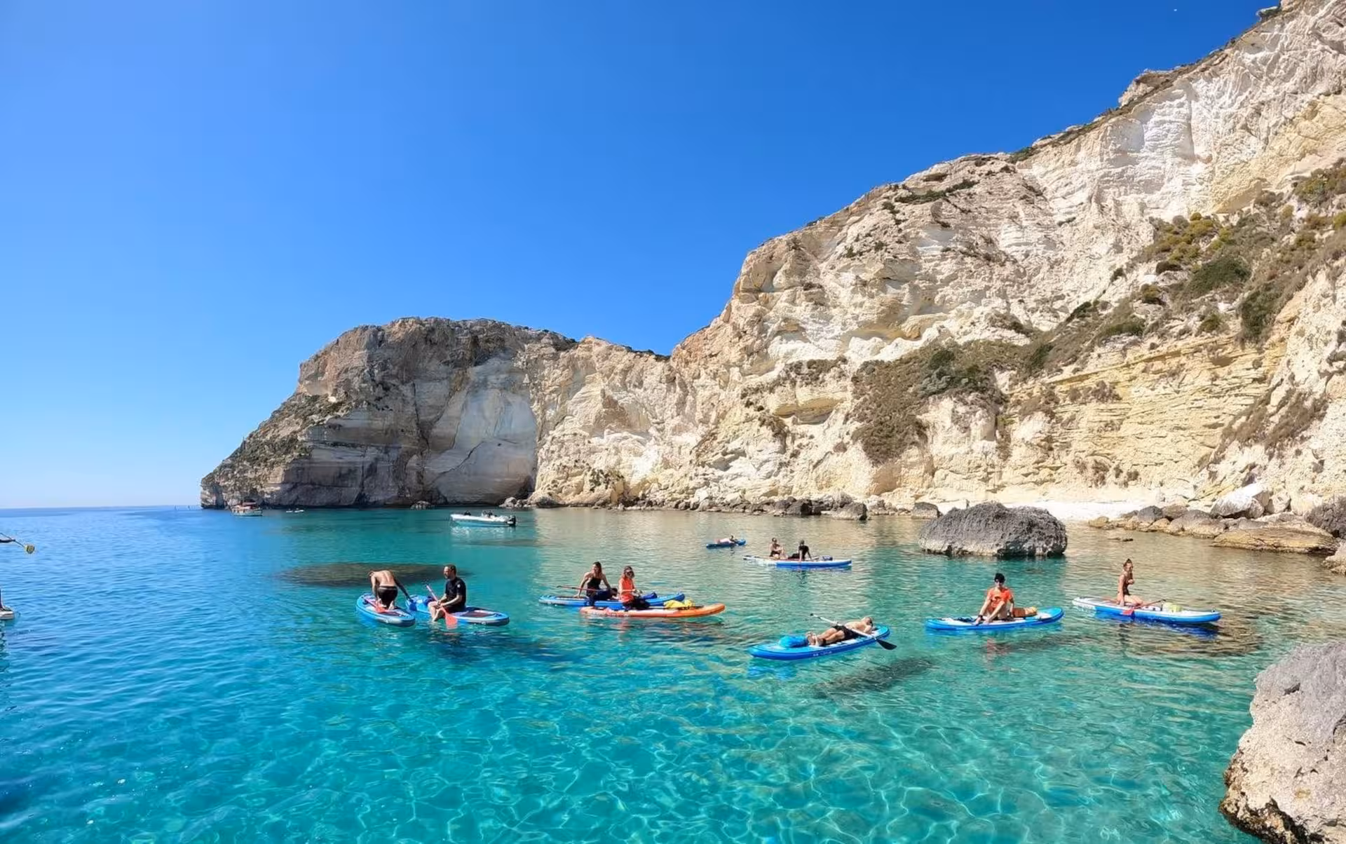 Paddleboarders enjoy crystal-clear waters at Sella del Diavolo on a sunny day during a Cagliari SUP and snorkeling tour.
