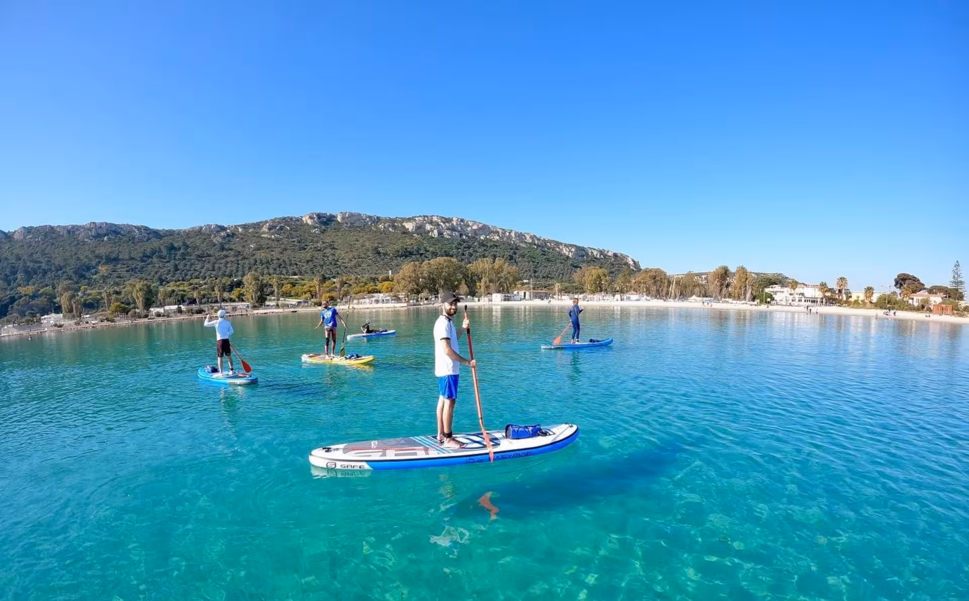 Group enjoying a stand-up paddleboarding tour on crystal-clear waters near Cagliari's Sella del Diavolo.