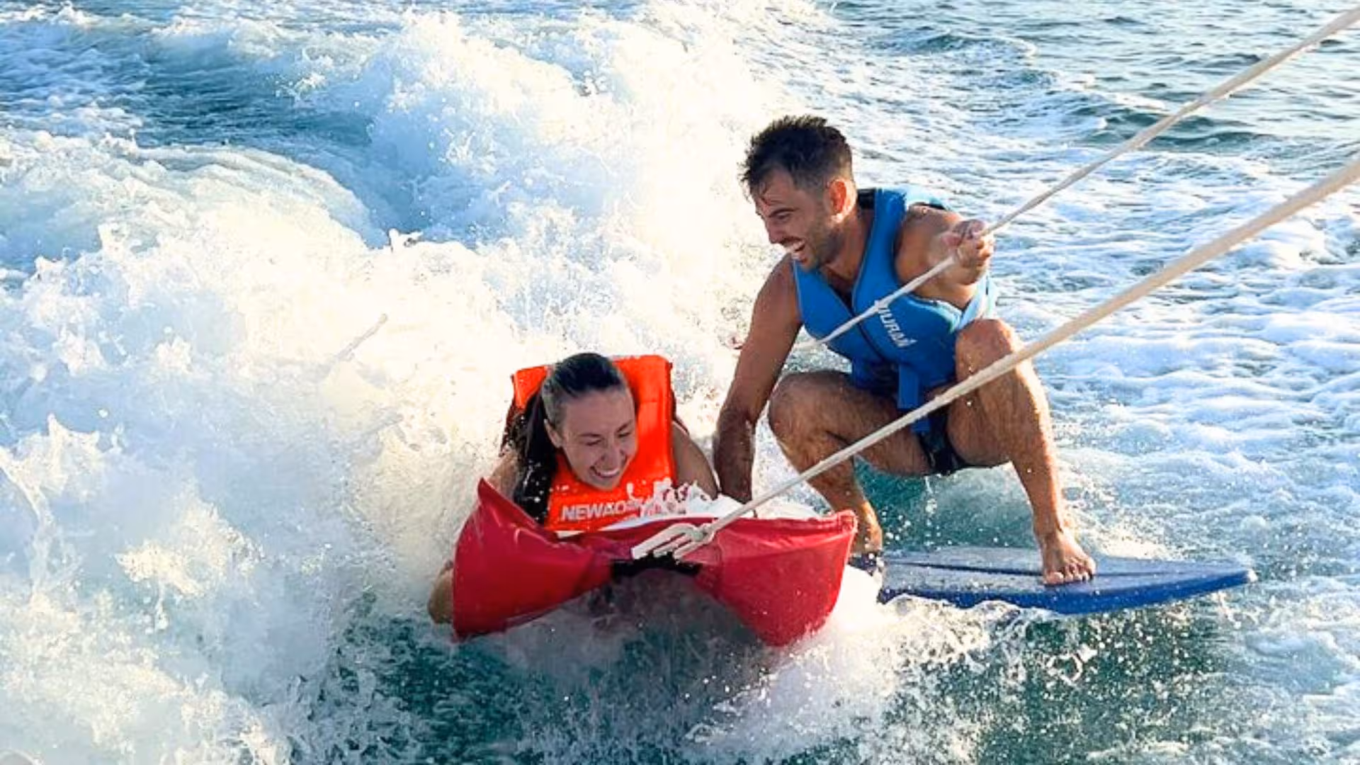 Two people enjoying thrilling water tubing in Golfo degli Angeli, Cagliari, with waves and smiles.