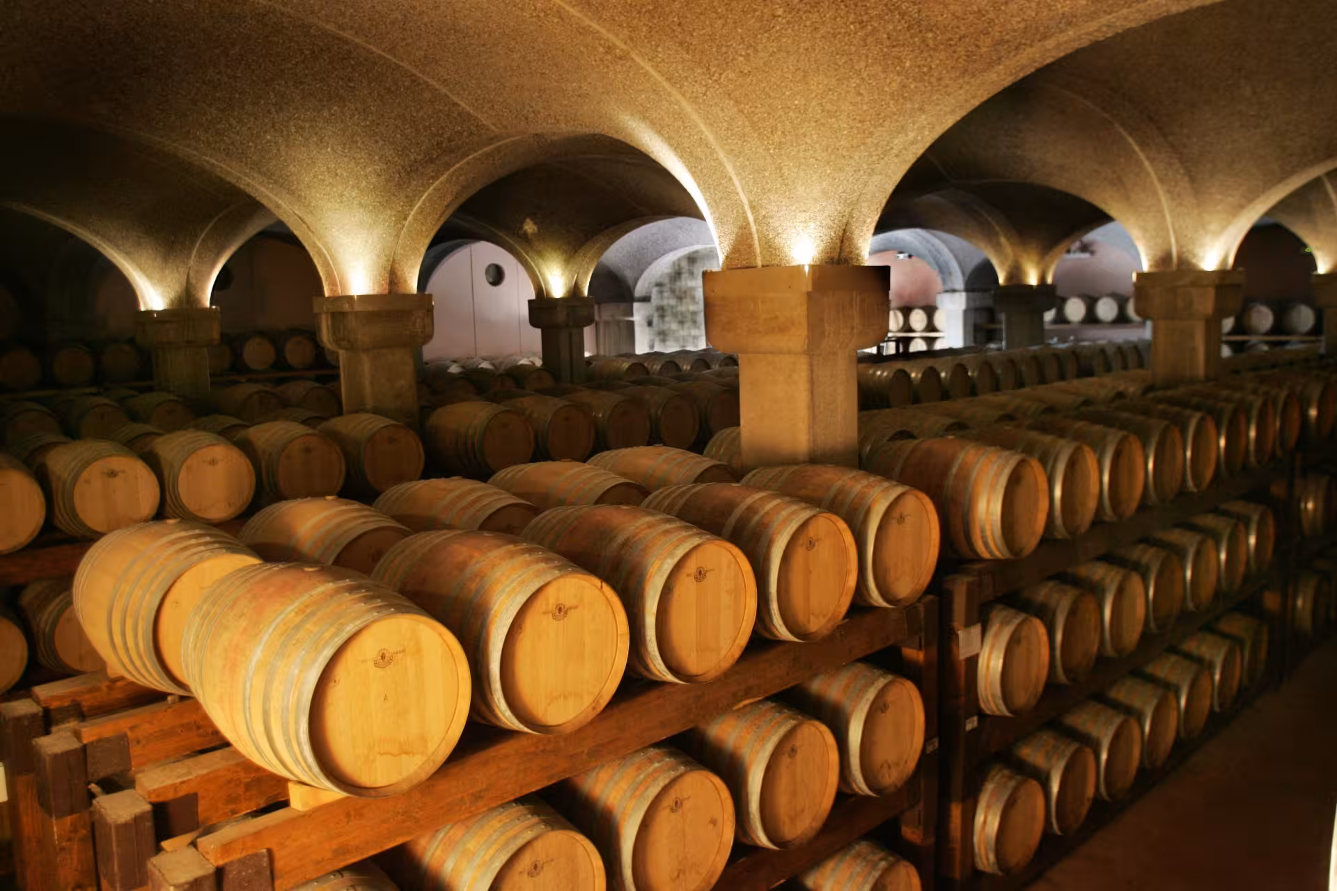 Underground wine cellar with rows of oak barrels in a Cagliari winery, ideal for wine tasting tours.