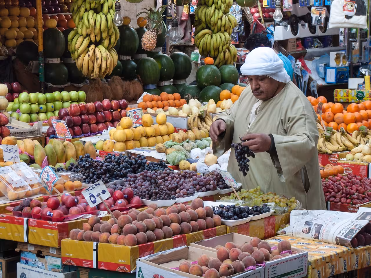 Egyptian vendor in traditional dress arranging colorful fresh fruits at Cairo bazaar market stall