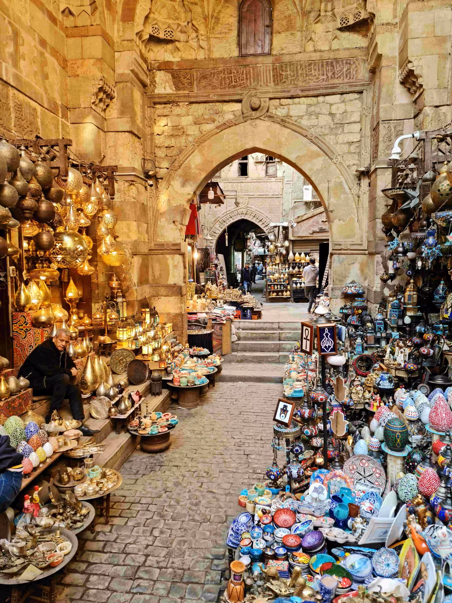 Colorful souvenirs and golden lanterns lining the stone archway passage of Cairo's Khan el-Khalili bazaar