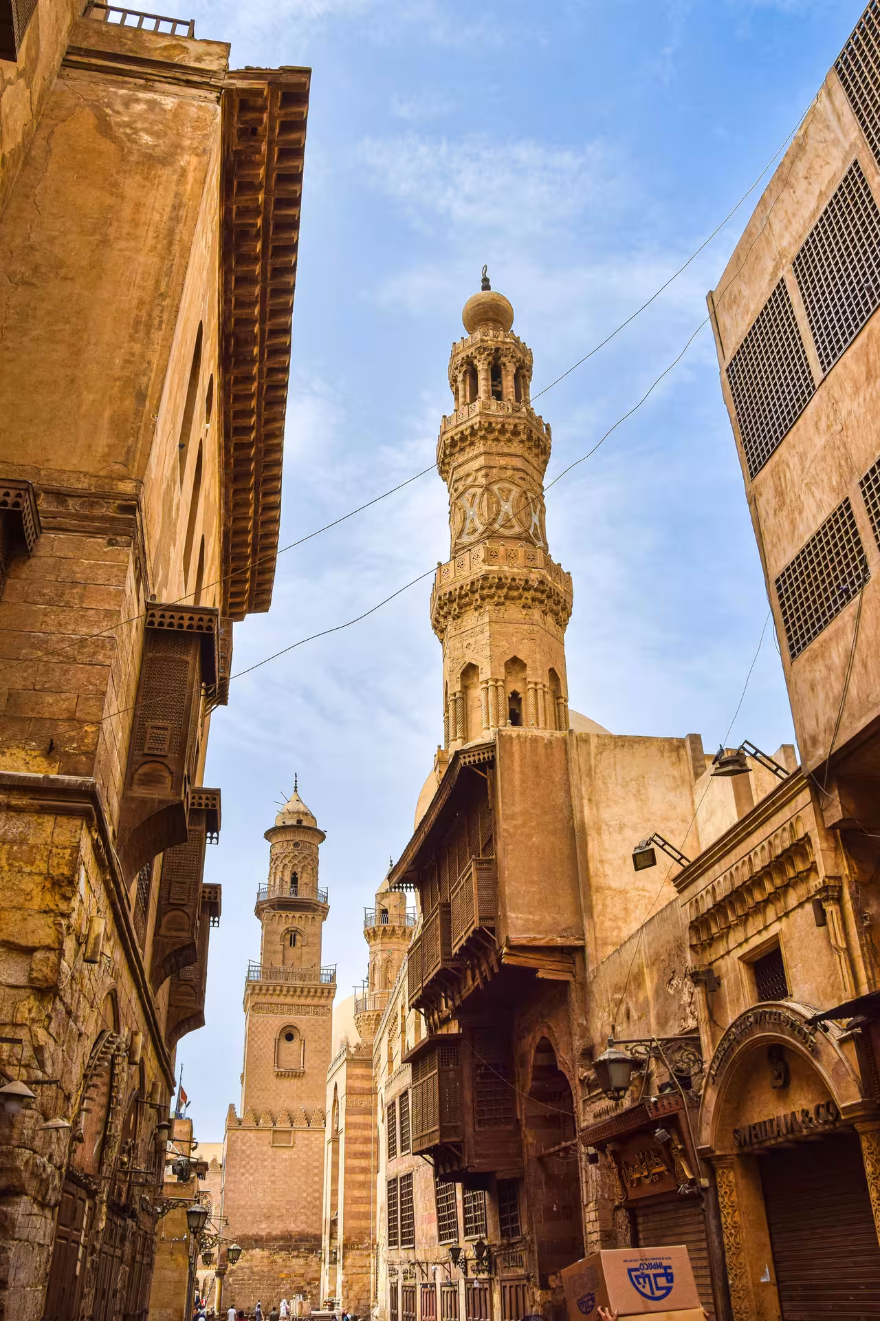 Medieval Islamic minarets and historic stone buildings along a narrow alley in Cairo Bazaar