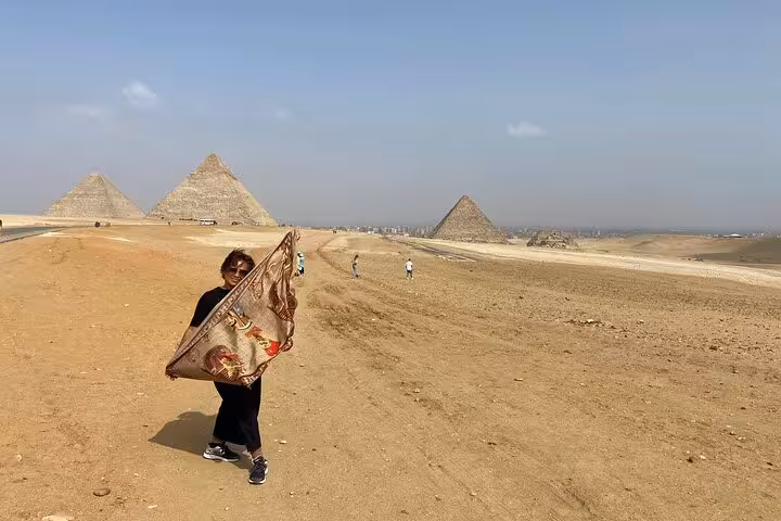 Traveler holding scarf with Giza Pyramids backdrop, part of Cairo camel ride, quad bike, lunch and shopping tour