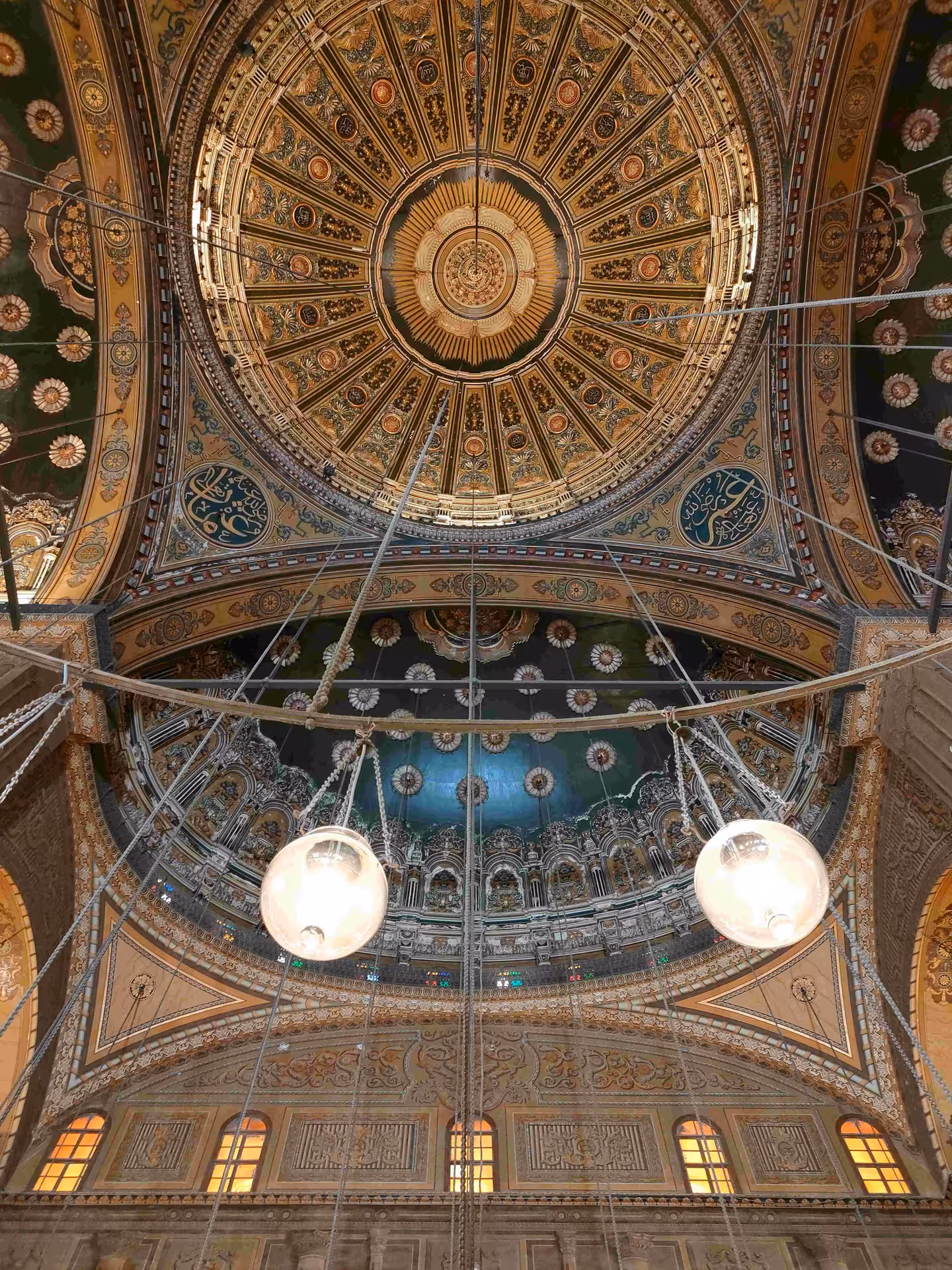 Ornate gilded dome ceiling with Islamic calligraphy and hanging lanterns inside Cairo Citadel mosque