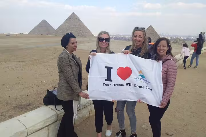 Tourists holding banner at Giza Pyramids viewpoint on Cairo day tour from Alexandria with desert panorama