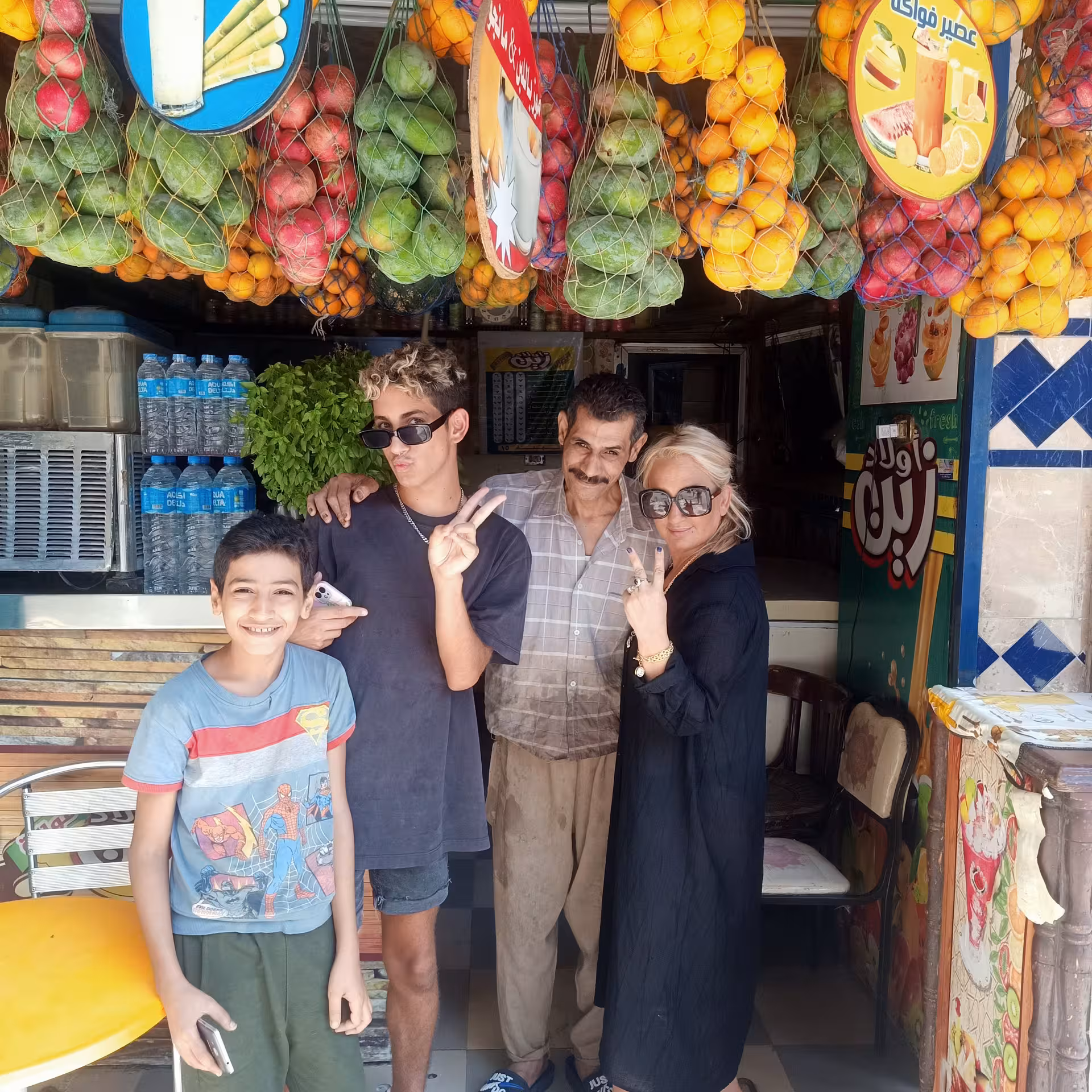 Group photo at a Cairo street juice shop with hanging fruit, part of a private food tour and funny walking tour