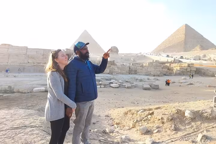 Couple with guide at Giza Plateau, pointing toward pyramids on Cairo 2-day tour including Pyramids and GEM