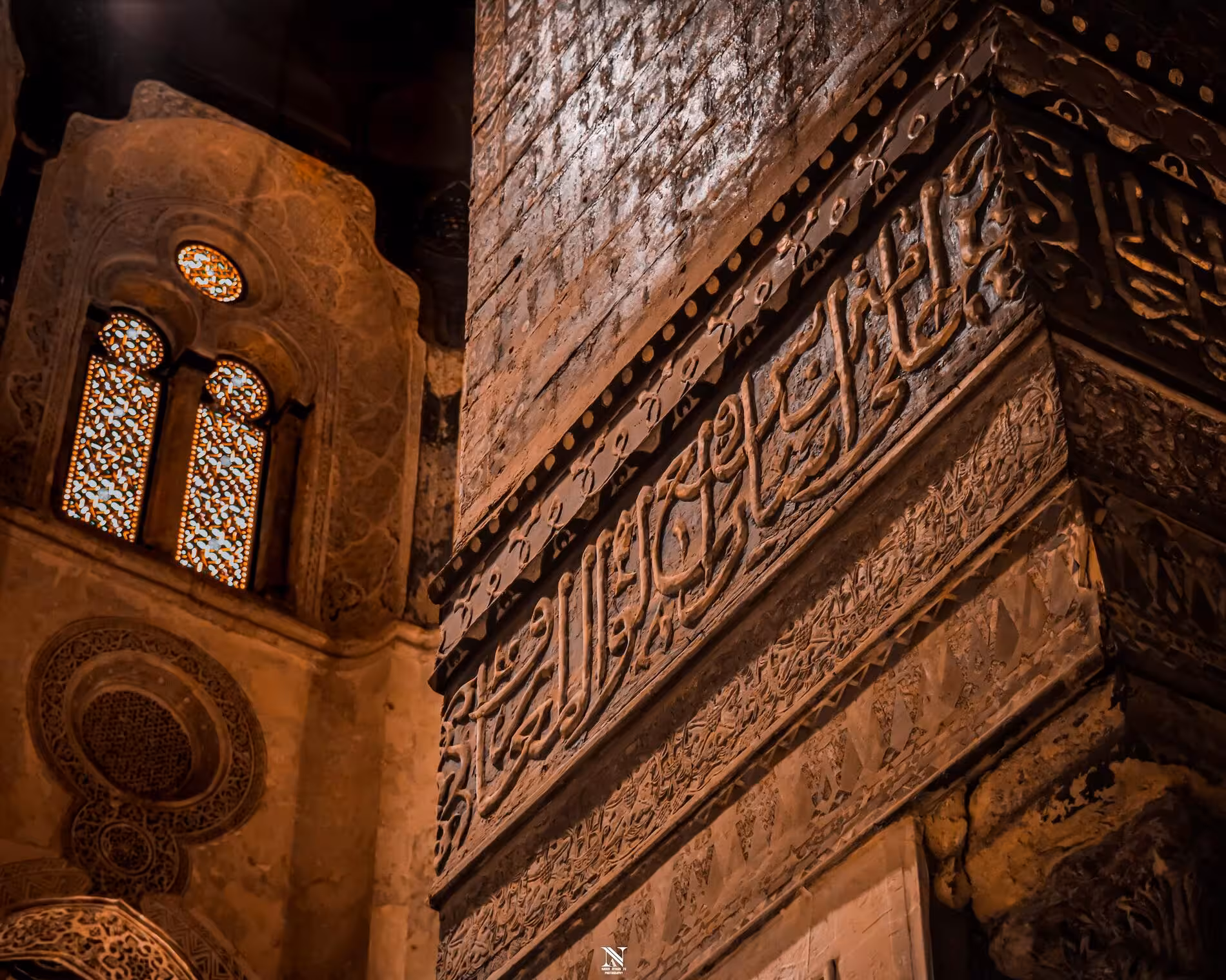 Intricate Arabic calligraphy carved in stone wall of historic Cairo mosque with ornate stained glass windows
