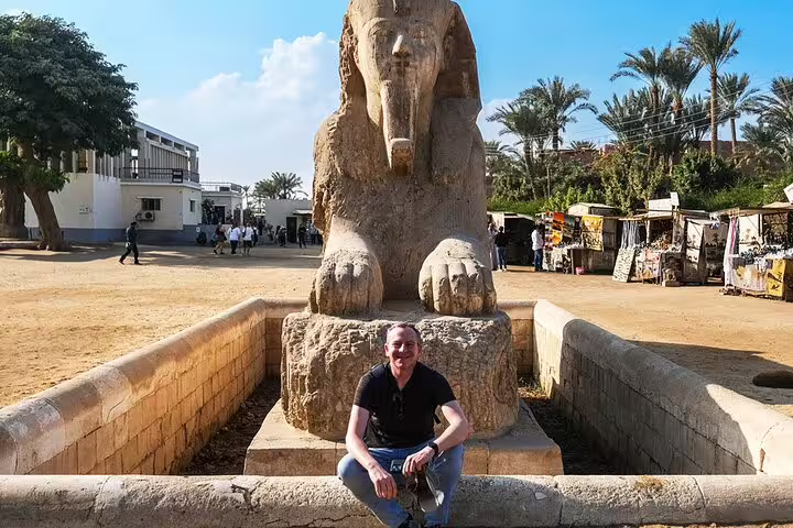 Traveler seated by ancient sphinx statue in Memphis on Cairo layover tour to Saqqara and Dahshur pyramids