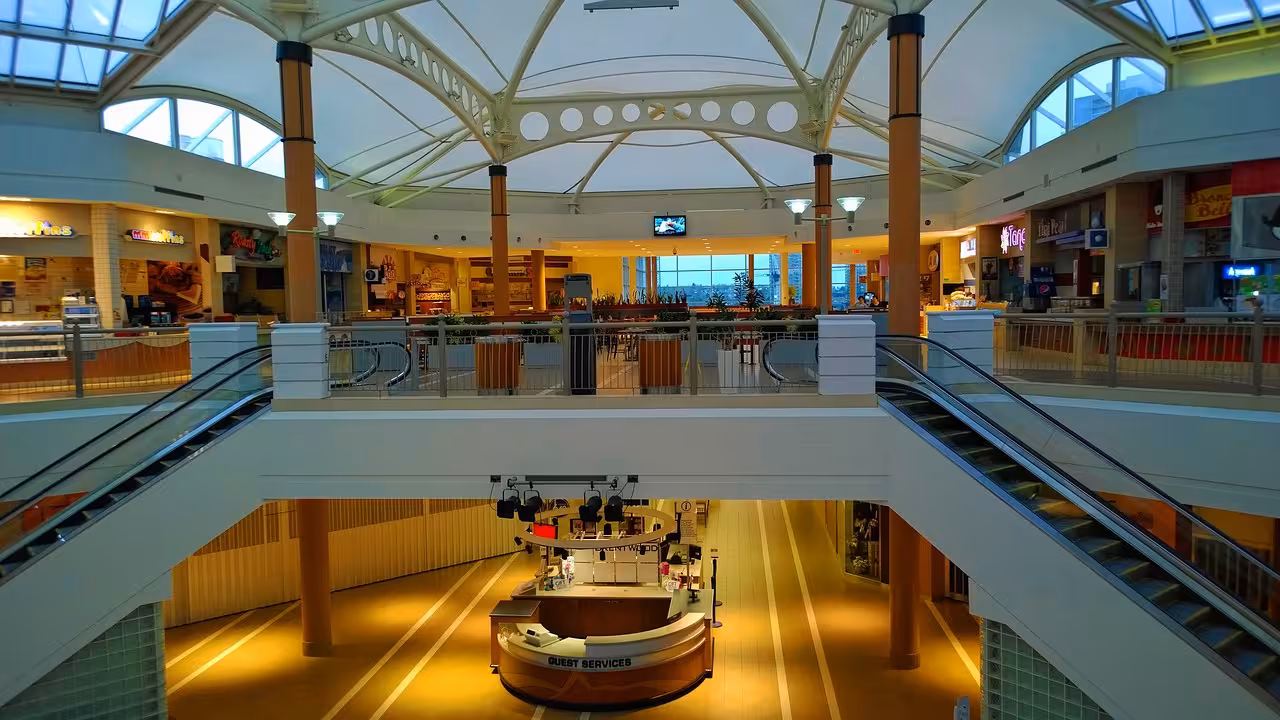 Modern multi-level shopping mall interior with escalators, food court, and guest services desk