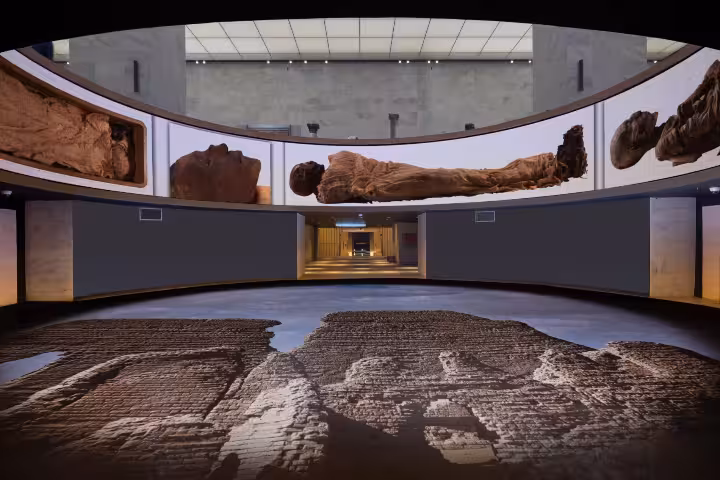 Cairo museum exhibit with Egyptian mummies displayed on curved screen above ancient inscribed floor