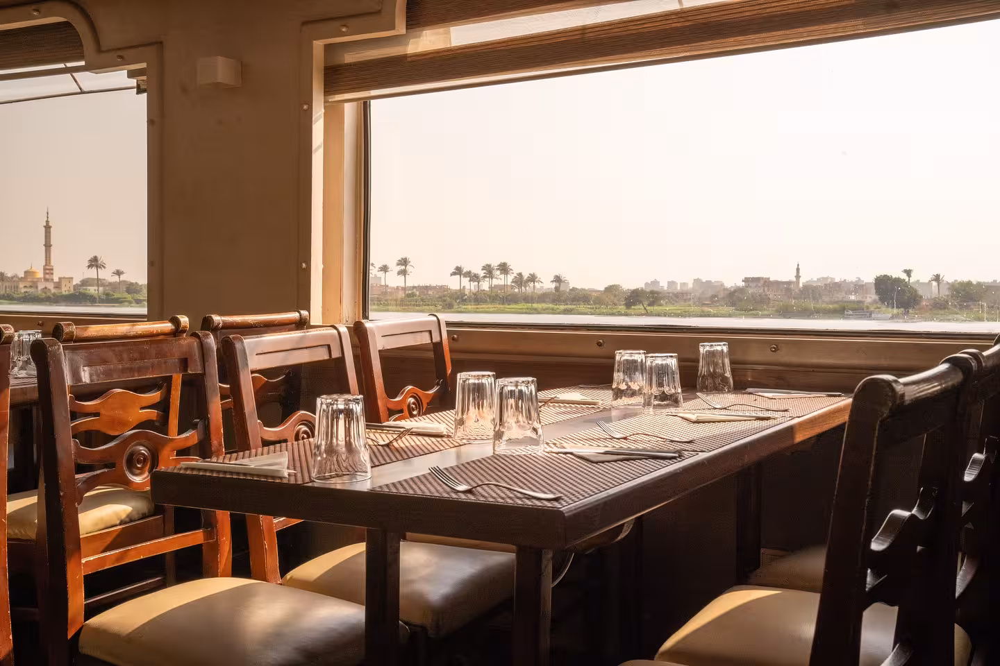Elegant dining table by panoramic window on deluxe Cairo Nile River dinner cruise at sunset with city views