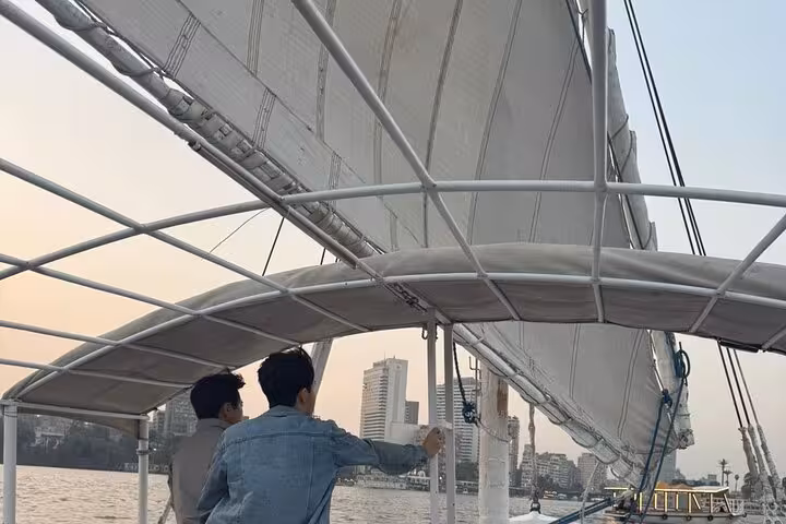 Travelers enjoy a Cairo Nile felucca ride beneath billowing sails, cruising past the city skyline at dusk
