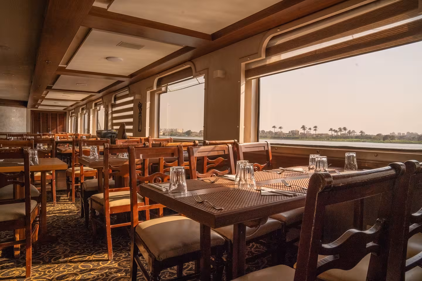 Deluxe Cairo Nile River dinner cruise dining room with panoramic windows, set tables, and sunset views