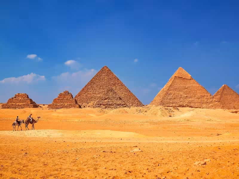 Camel riders crossing desert with the Pyramids of Giza on a Cairo private tour to Memphis Saqqara with lunch