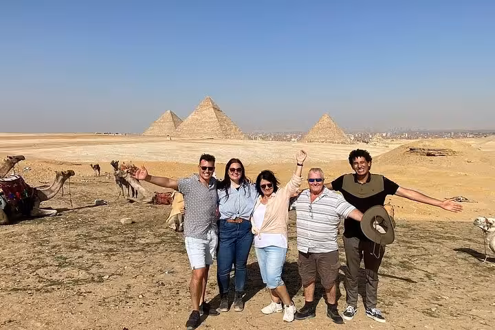 Private Cairo tour group posing with camels and the Pyramids of Giza in the background, Egyptian lunch included