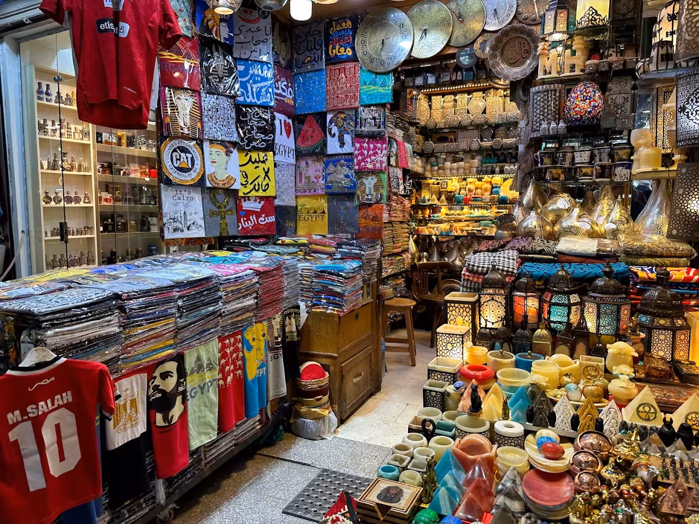 Colorful Cairo souq stall selling Egyptian souvenirs, t-shirts, lanterns, and decorative plates at Khan el-Khalili market