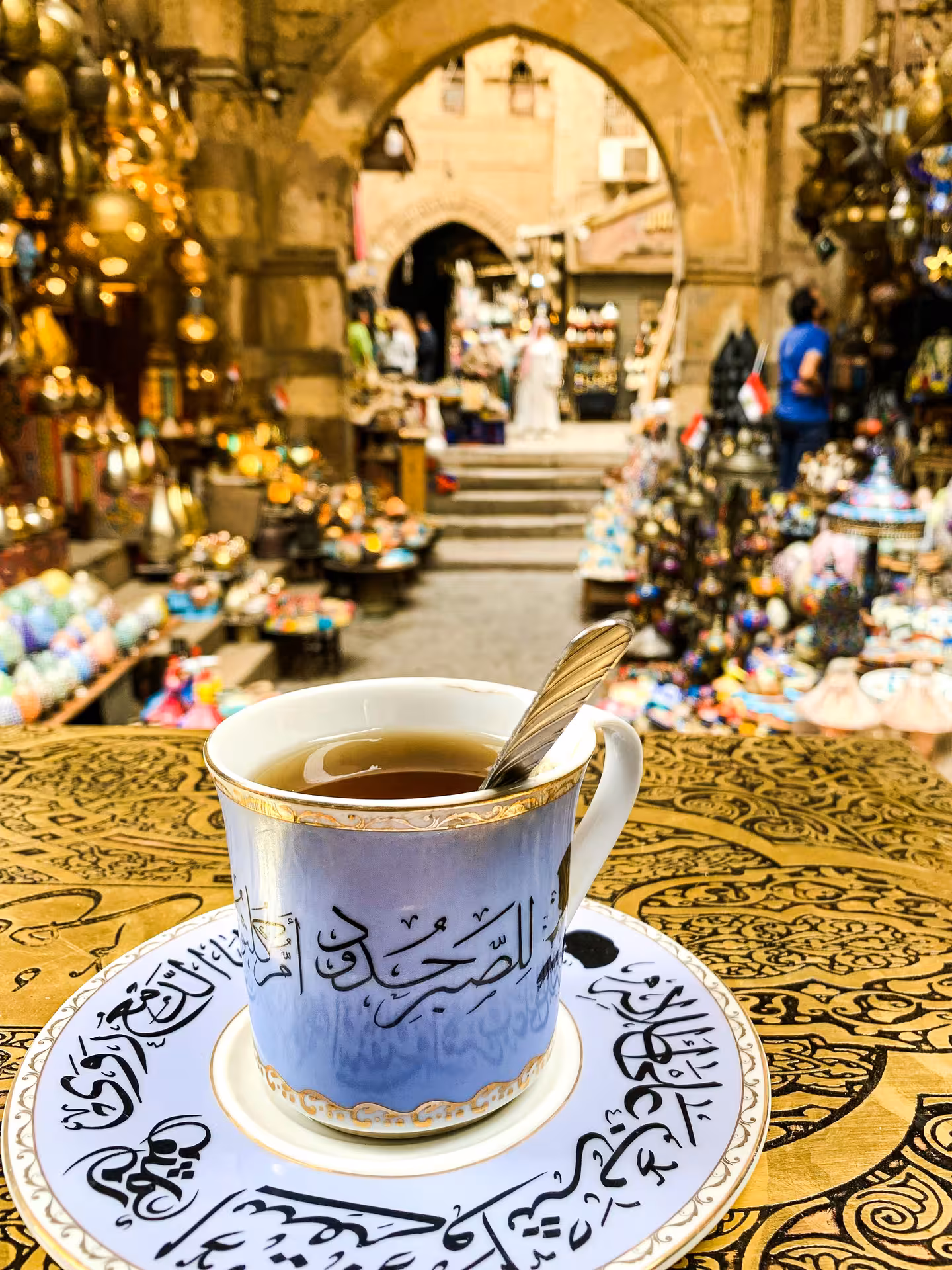 Arabic calligraphy tea cup at Khan el-Khalili souq market in Cairo with golden lanterns and archway