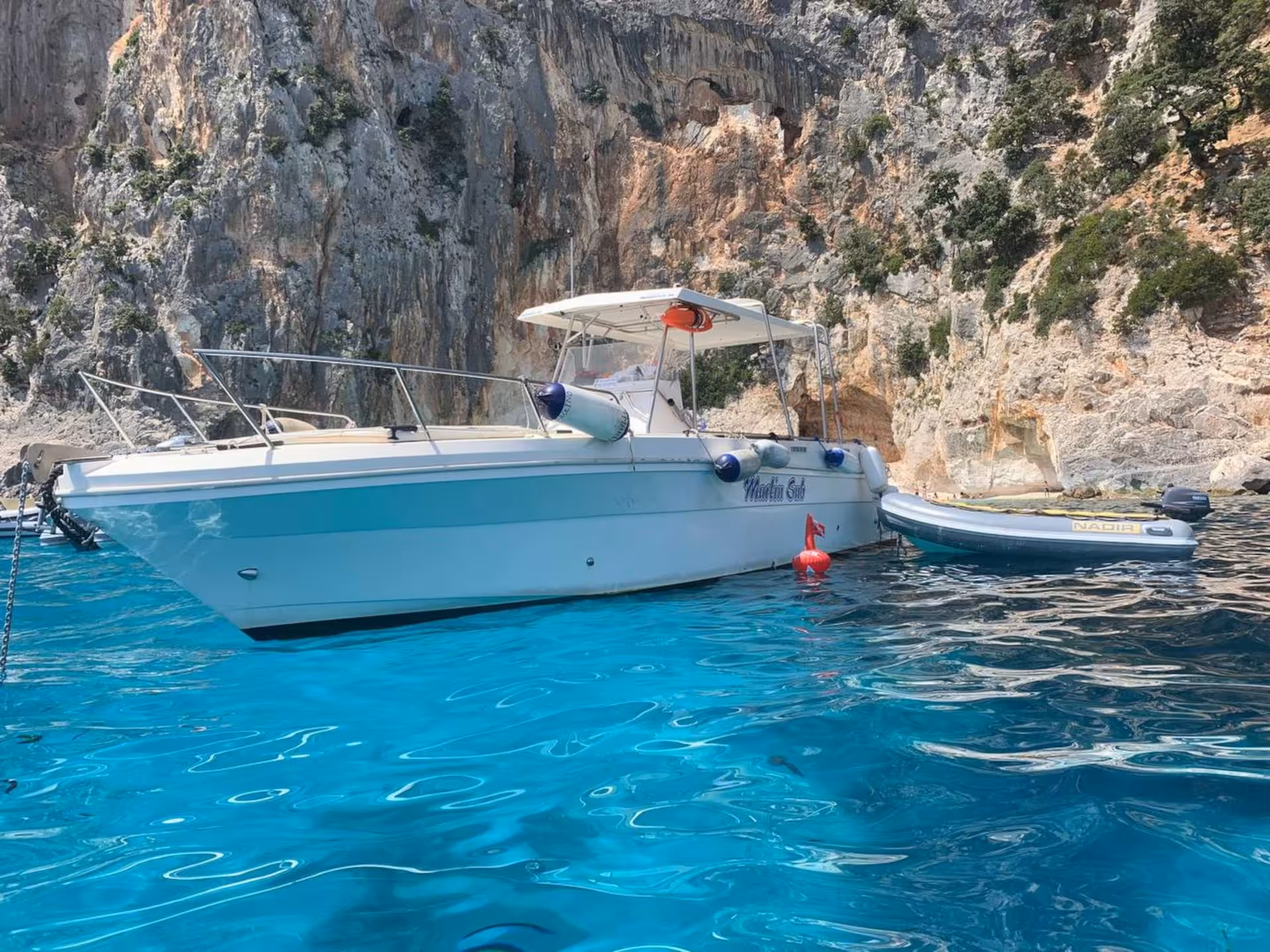 White boat anchored in the crystal-clear waters of the Gulf of Orosei, with rocky cliffs in the background.