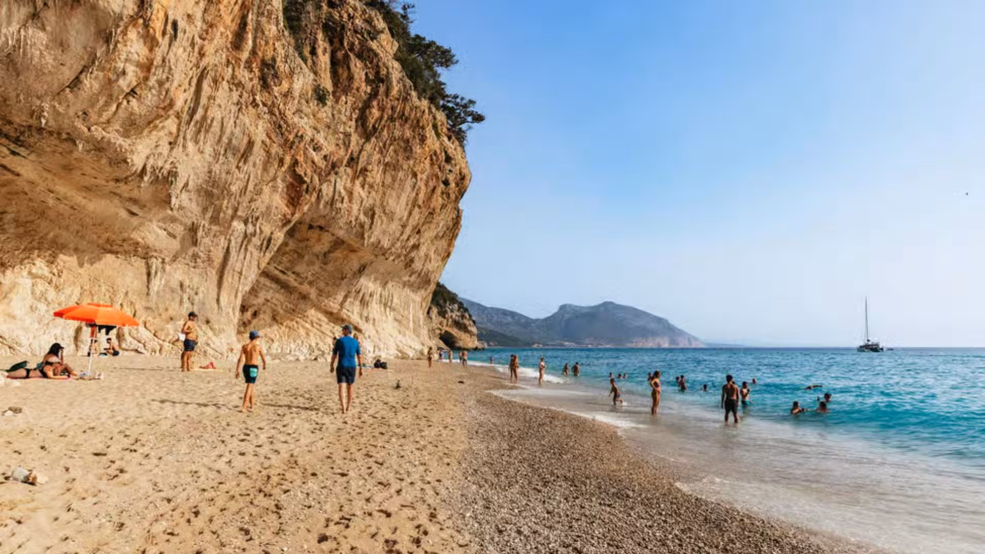 Visitors enjoy a sunny day on a sandy beach with rocky cliffs in the Gulf of Orosei, perfect for a dinghy trip.