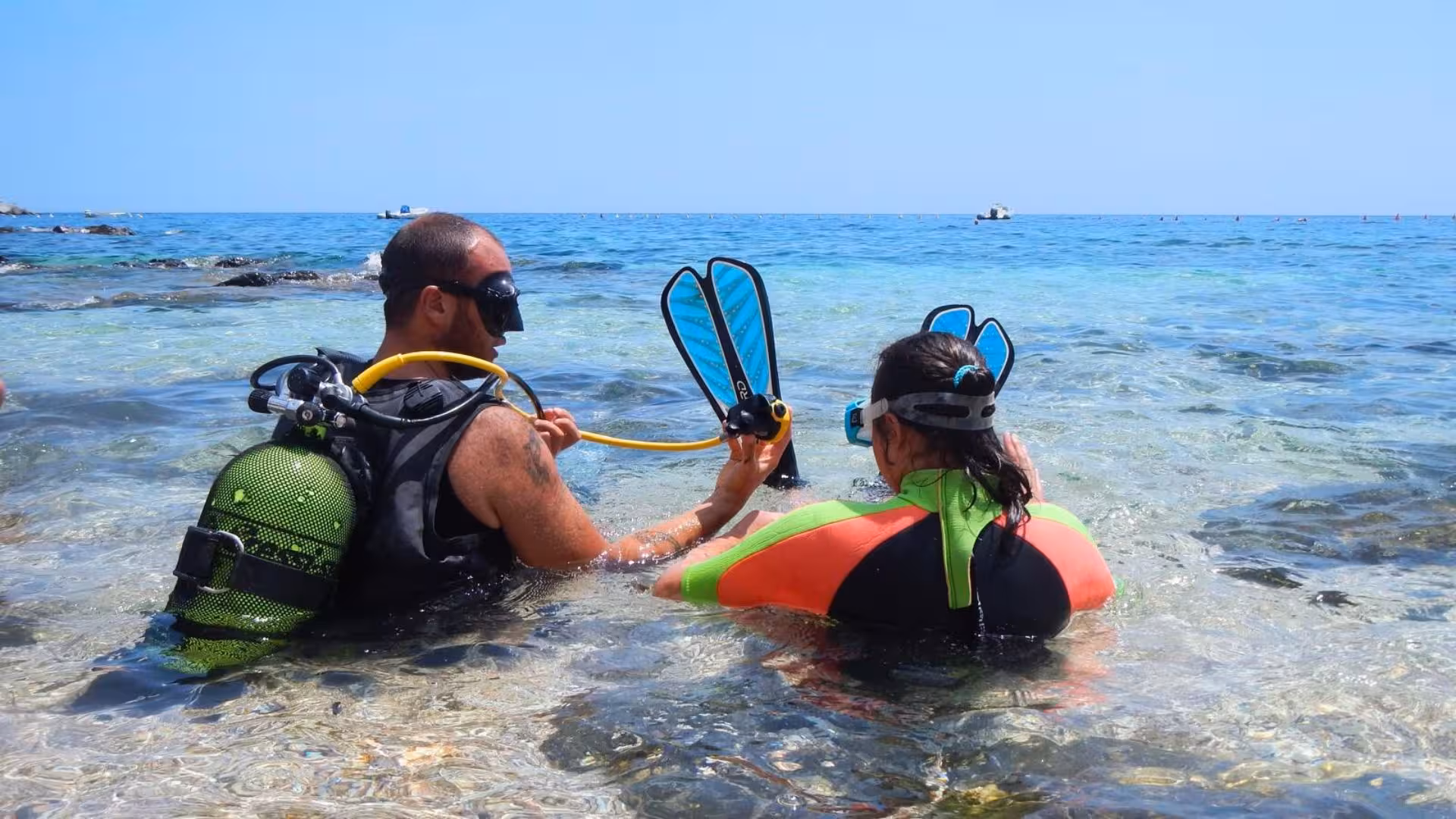 Diving instructor prepares student for underwater baptism in Cala Gonone's stunning crystal-clear waters.