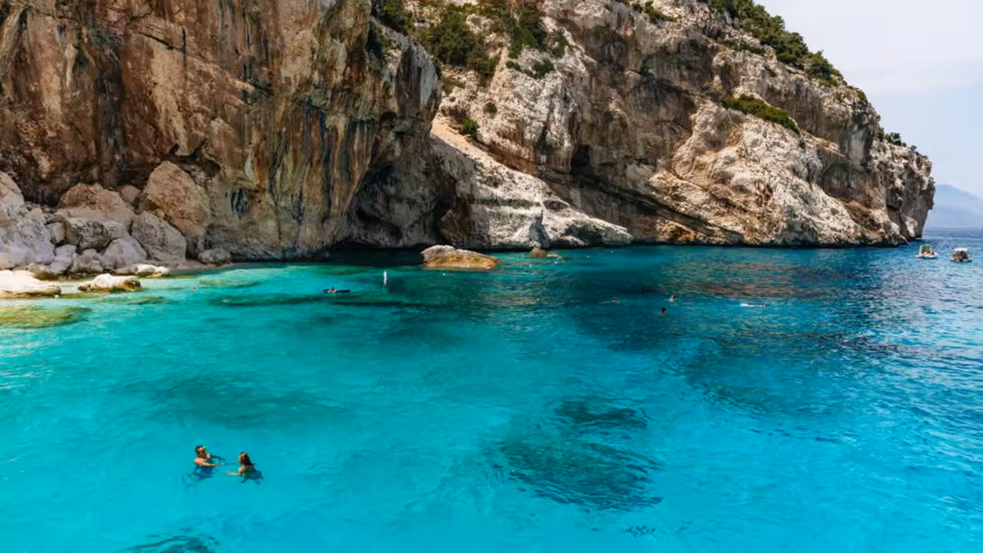 Swimmers enjoy the crystal-clear waters near Cala Gonone's rocky cliffs in the Gulf of Orosei.