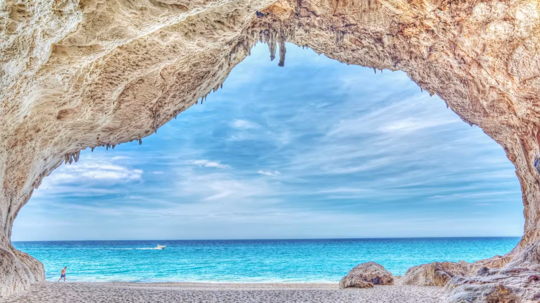 View from a rocky cave opening to a pristine beach and turquoise sea in the Gulf of Orosei, Cala Gonone.