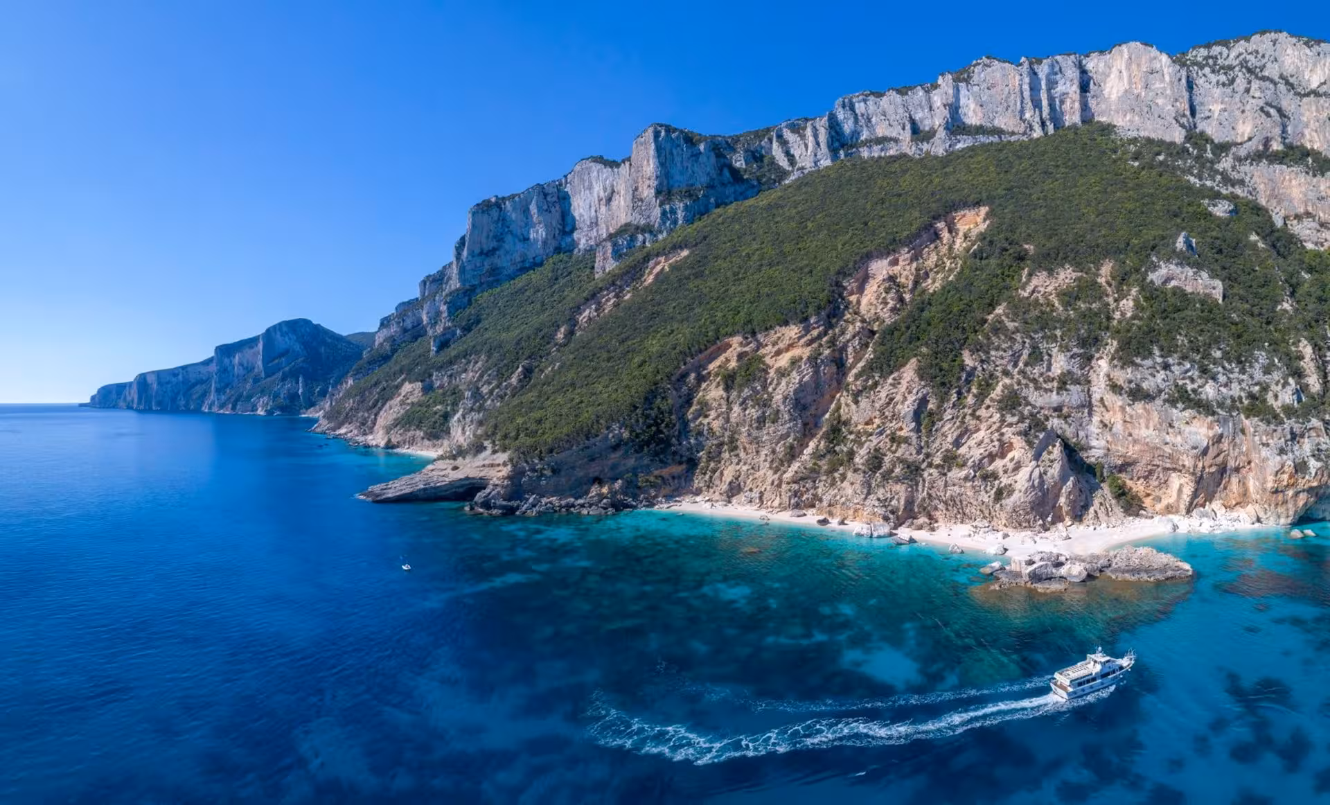 Aerial view of motorboat cruising along the majestic coastline of Cala Gonone towards Bue Marino Caves.