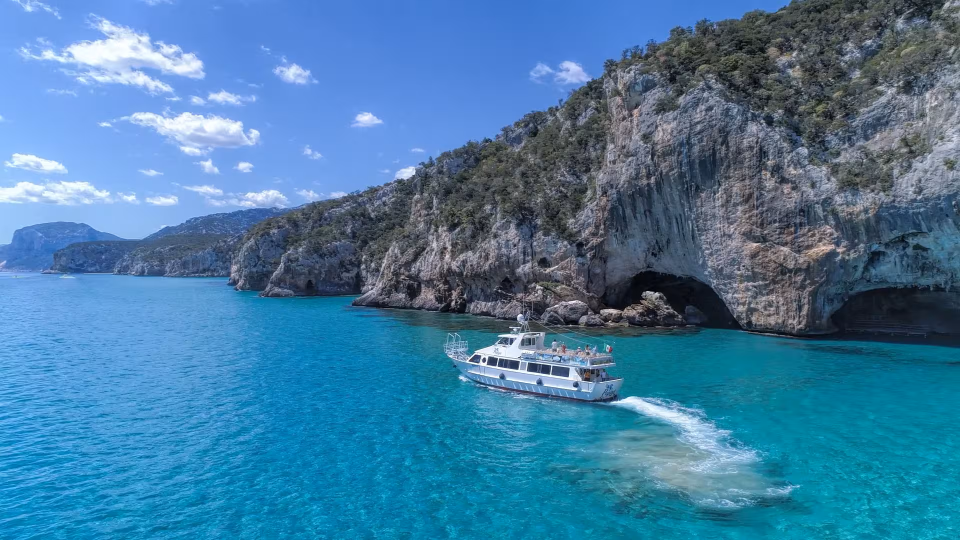 Motorboat cruising near the dramatic cliffs and caves of Cala Luna, offering breathtaking views on a Cala Gonone tour.
