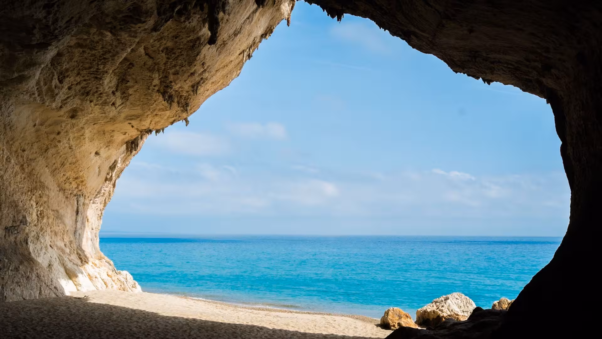 View from a cave opening to the turquoise sea and sandy beach in Cala Gonone, ideal for RIB rentals.